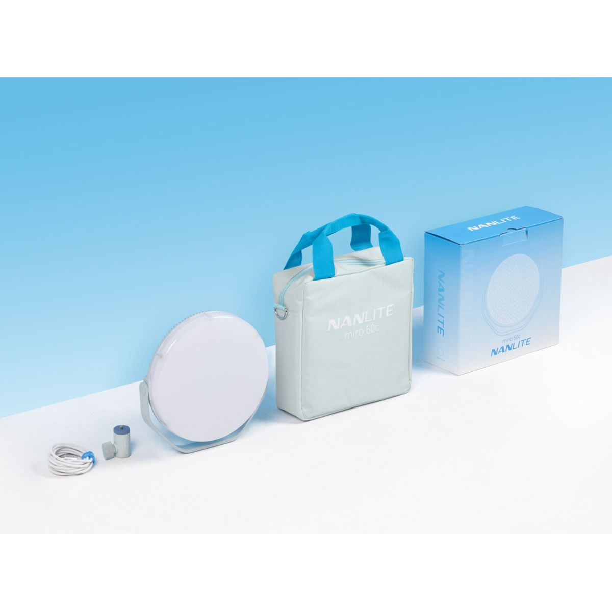 Una luce LED Nanlite bianca, borsa e scatola su una superficie bianca con sfondo sfumato blu.