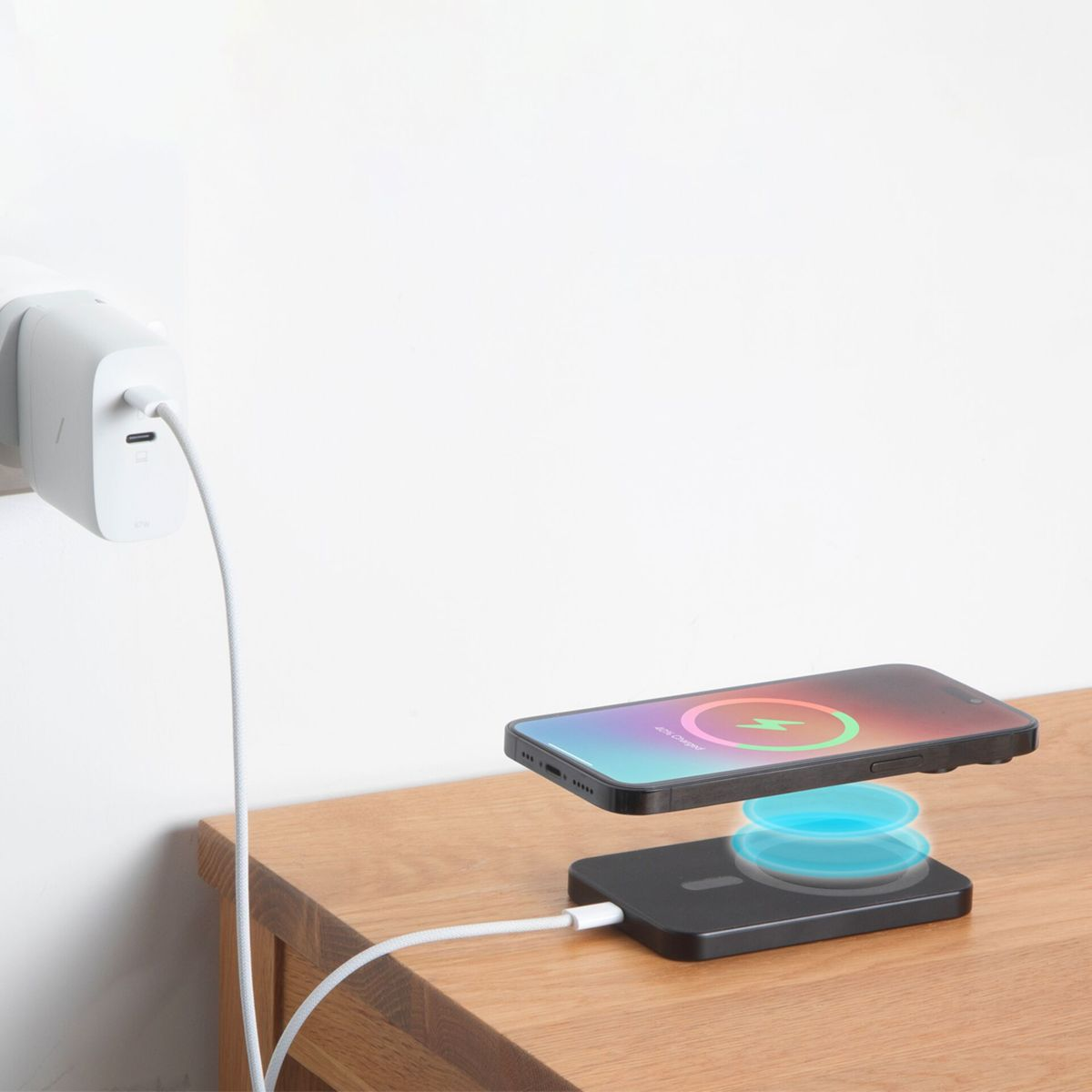 Ein Telefon wird kabellos auf einem schwarzen Ladepad aufgeladen. Ein weißes Kabel ist mit dem Pad und einem Wandladegerät verbunden.