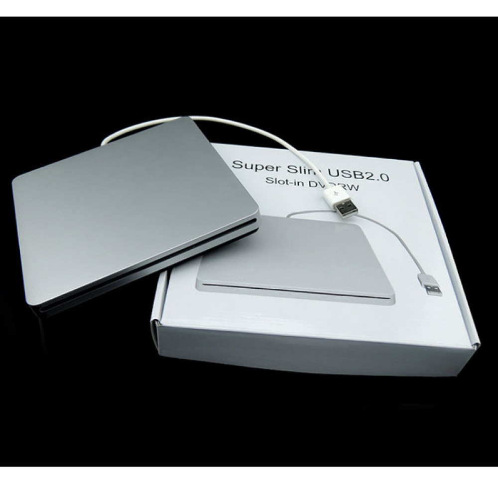 Ein silbernes externes DVD-Laufwerk mit USB-Kabel liegt auf einem weißen Karton. Der Karton hat Text. Der Hintergrund ist schwarz.