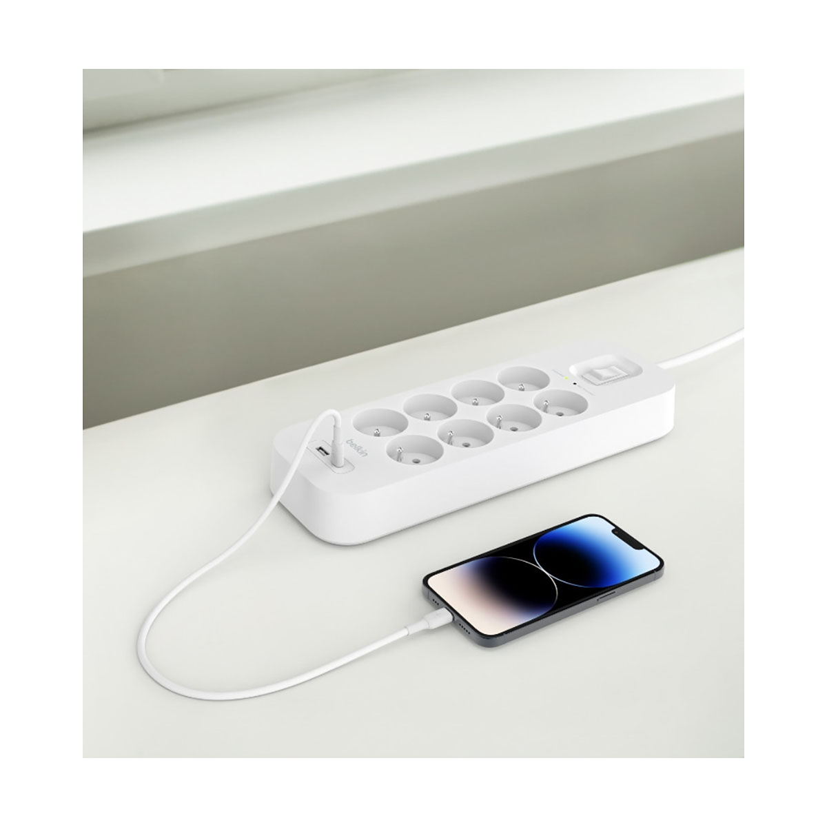 Multipresa bianca con telefono collegato. Il telefono è nero e ha un cavo di ricarica bianco.
