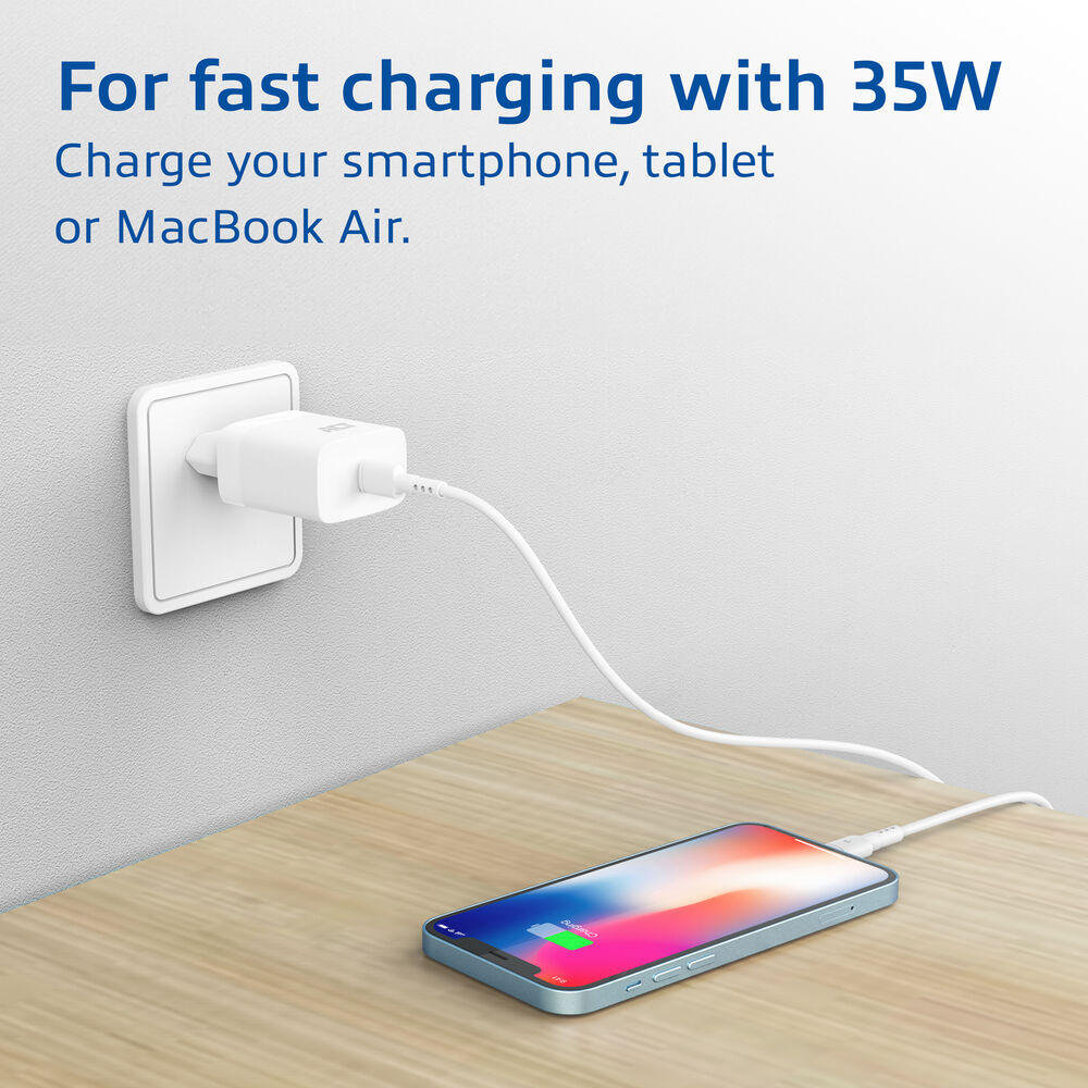 Un téléphone se recharge sur une table en bois. Un chargeur blanc est branché au mur. L'écran affiche la charge.