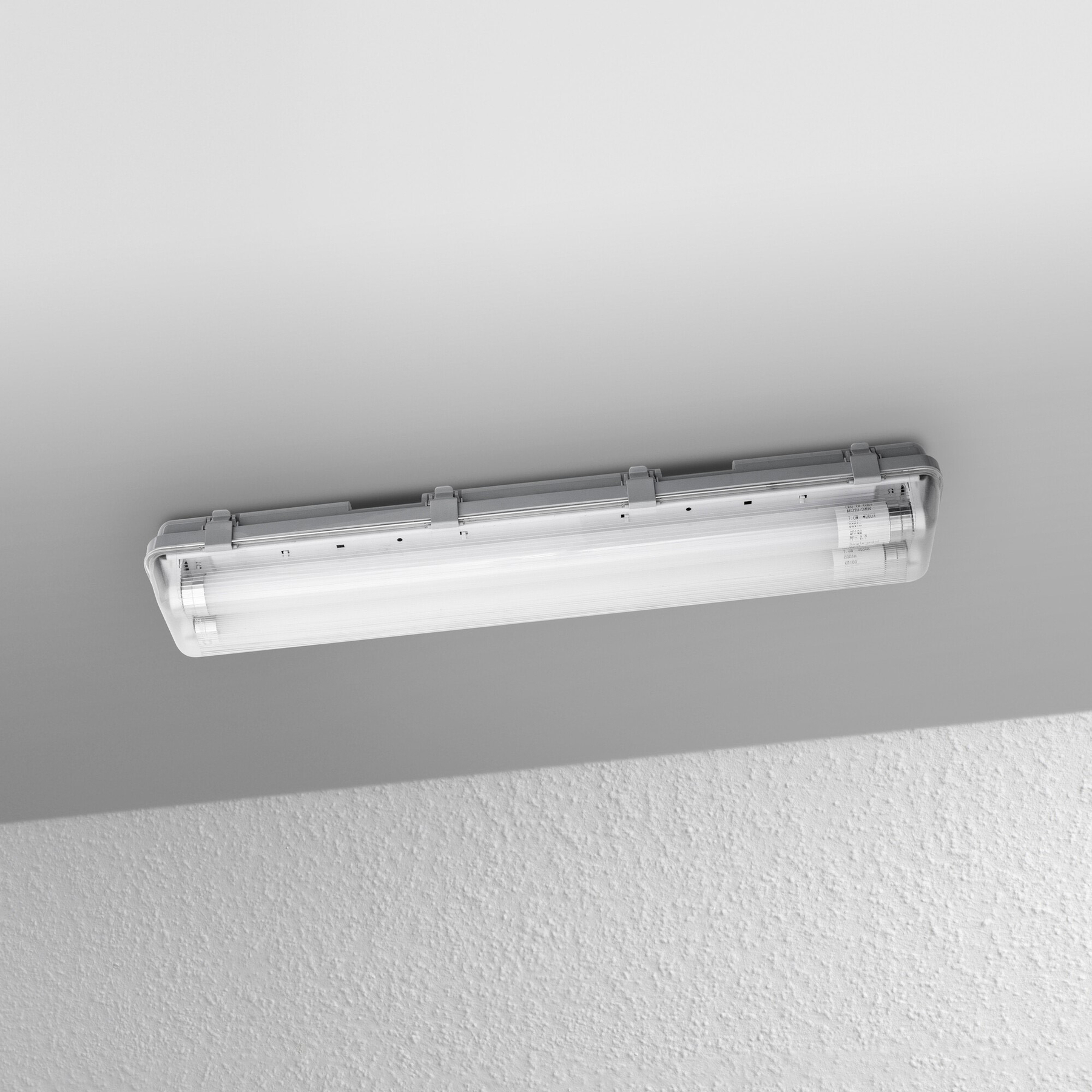 Eine Leuchtstoffröhre ist an der Decke montiert. Die Decke ist weiß, und die Wand darunter ist strukturiert weiß.