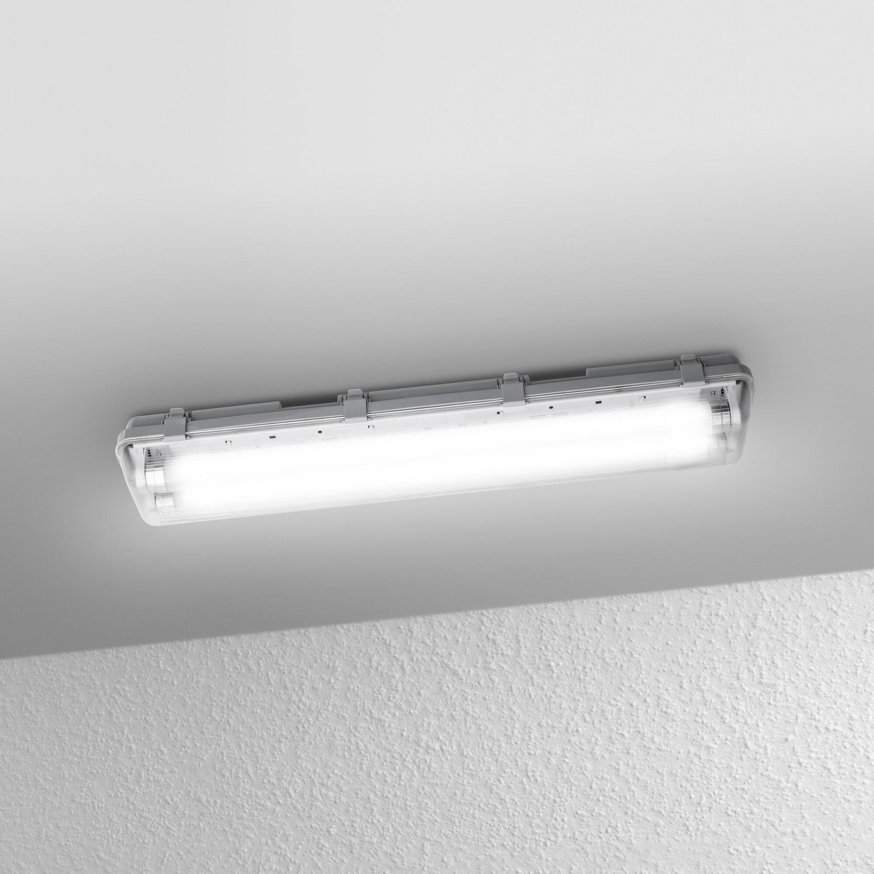 Eine Leuchtstoffröhre ist an der Decke befestigt. Das Licht ist an und beleuchtet die weiße Decke. Darunter eine strukturierte Wand.