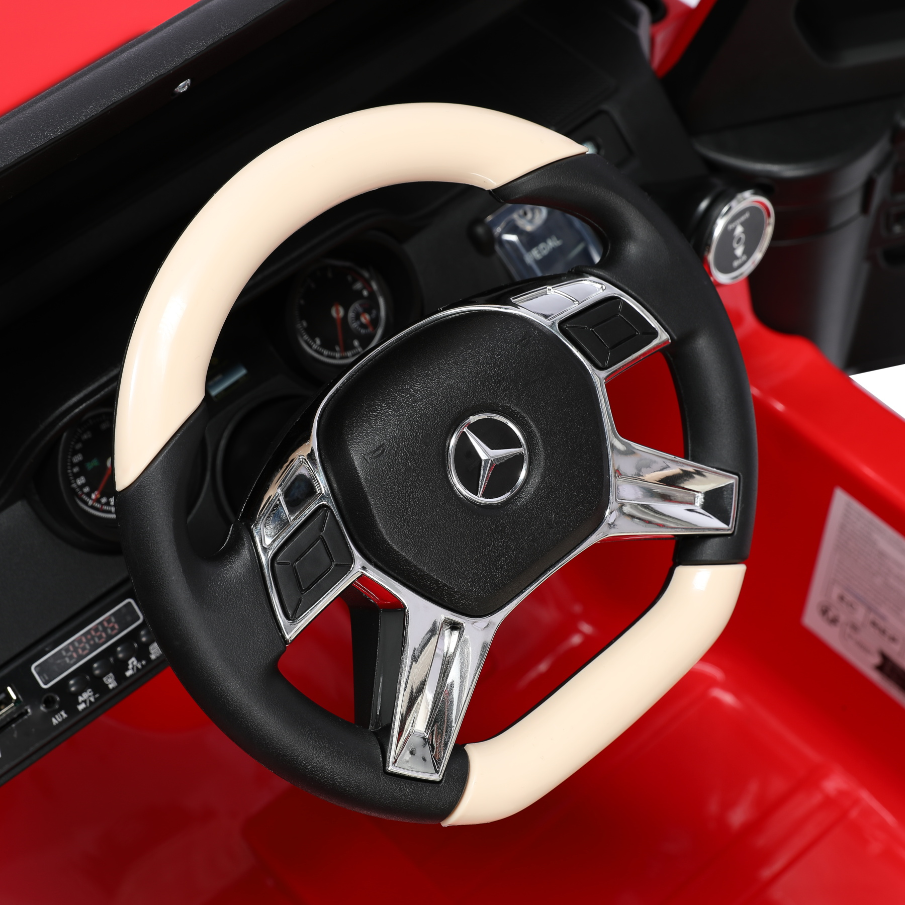 Nahaufnahme des Lenkrads eines roten Spielzeugautos mit beigem Rand und schwarzer Mitte, Mercedes-Logo.