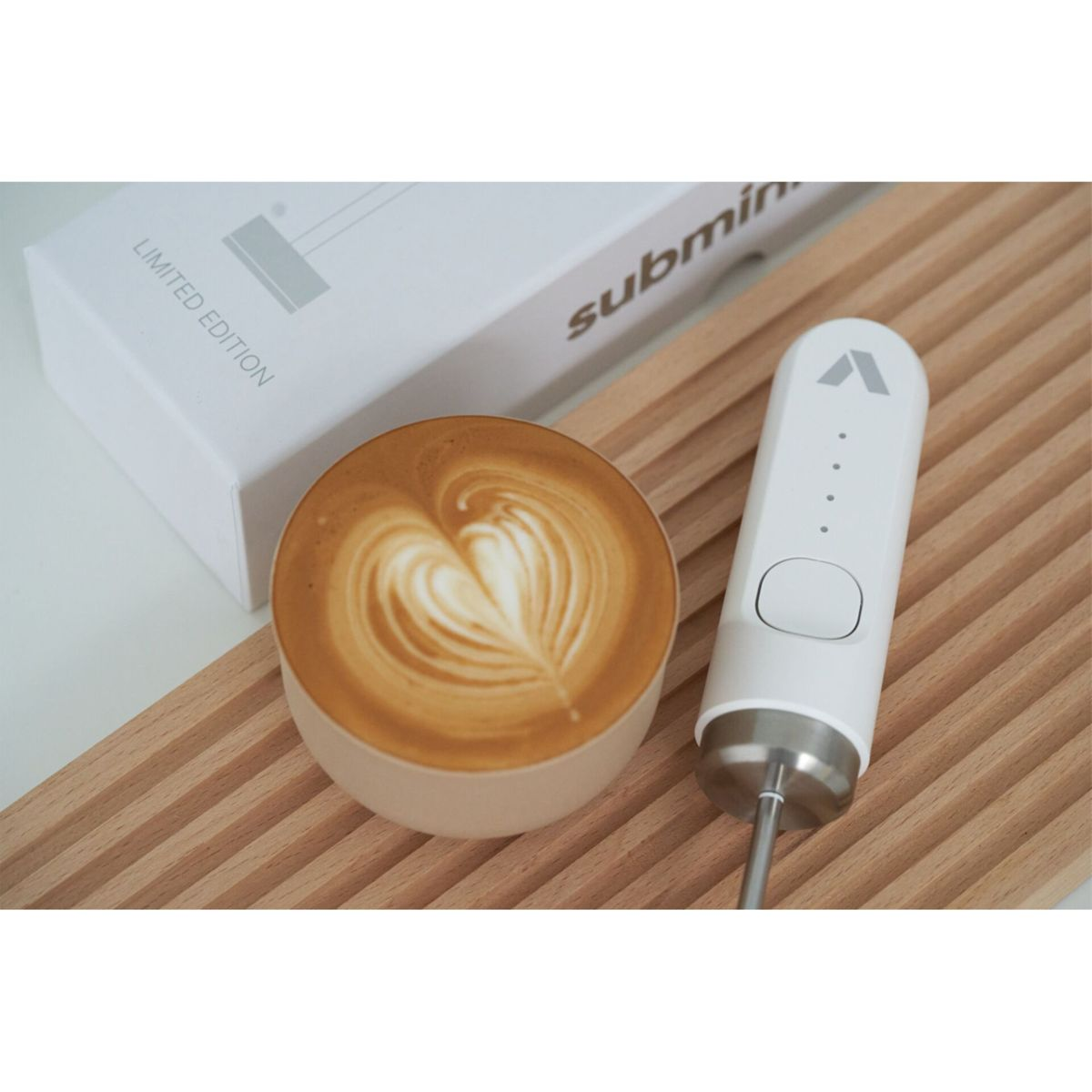 Ein Latte mit Herz-Kunst, ein weißer Milchaufschäumer und eine 'Limited Edition'-Box liegen auf einem Holzbrett.