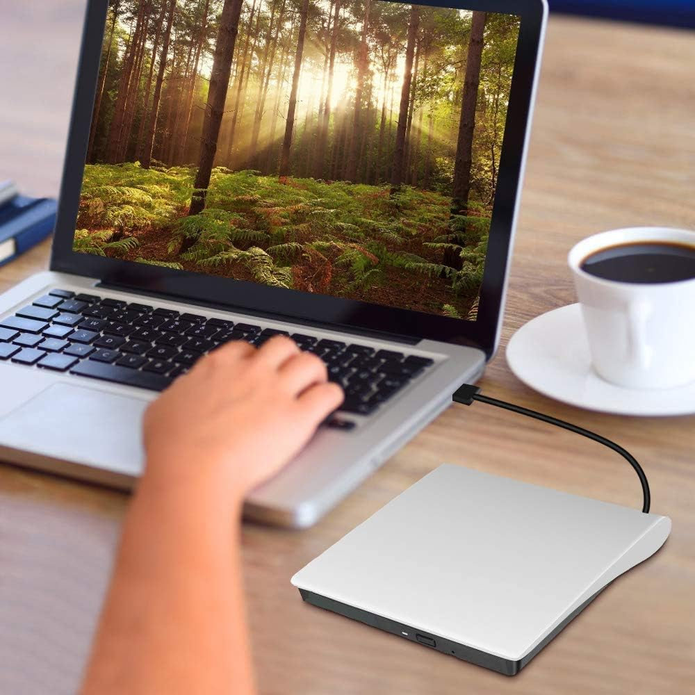 Ein Laptop zeigt eine Waldszene. Eine Hand tippt. Eine Kaffeetasse und ein externes Laufwerk liegen auf dem Tisch.