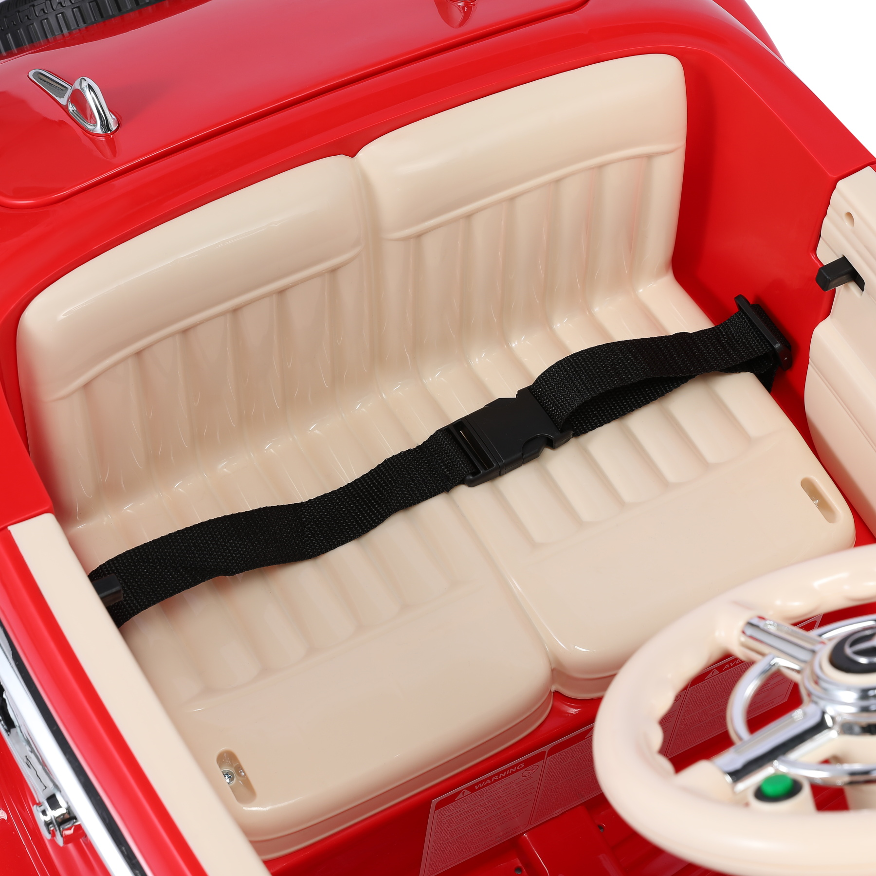 Roter Spielzeugauto-Innenraum mit cremefarbenen Sitzen, schwarzem Sicherheitsgurt und Lenkrad. Warnhinweis sichtbar.