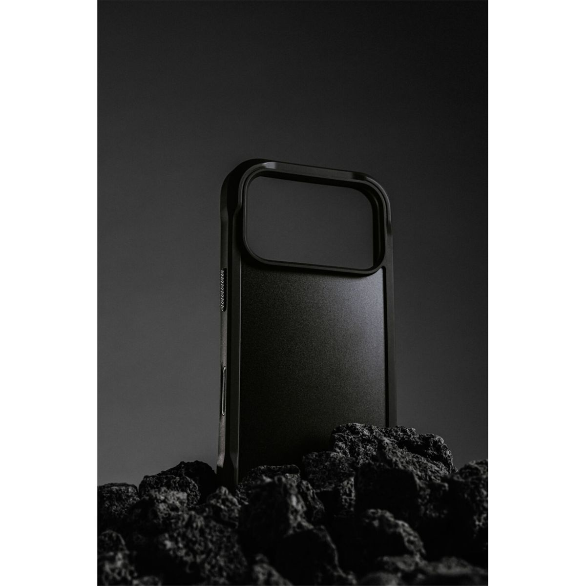 Una custodia nera per telefono poggia su rocce scure. La custodia ha un ritaglio per la fotocamera e una superficie strutturata. Lo sfondo è scuro.