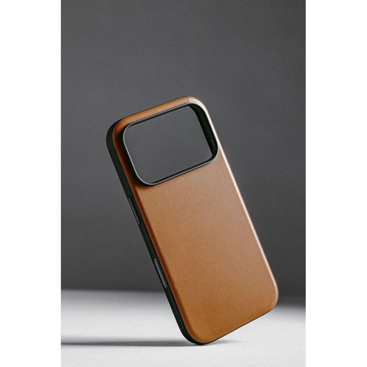 Una custodia per telefono marrone con un ritaglio nero per la fotocamera è inclinata su uno sfondo grigio. La custodia ha una trama liscia e un telaio scuro.
