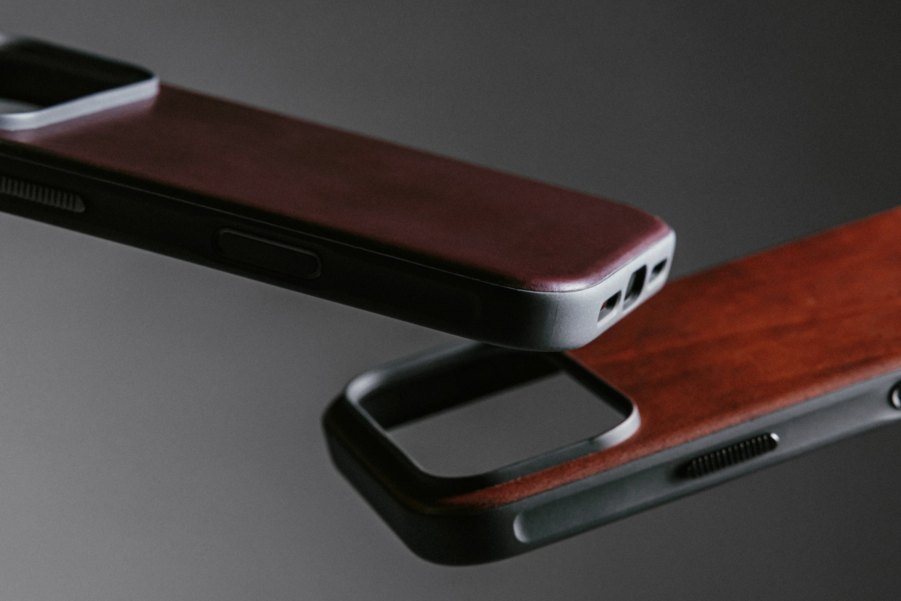 Due custodie per telefoni, una sopra l'altra. Entrambe hanno una texture in legno e bordi neri, con fori per la fotocamera e i pulsanti.
