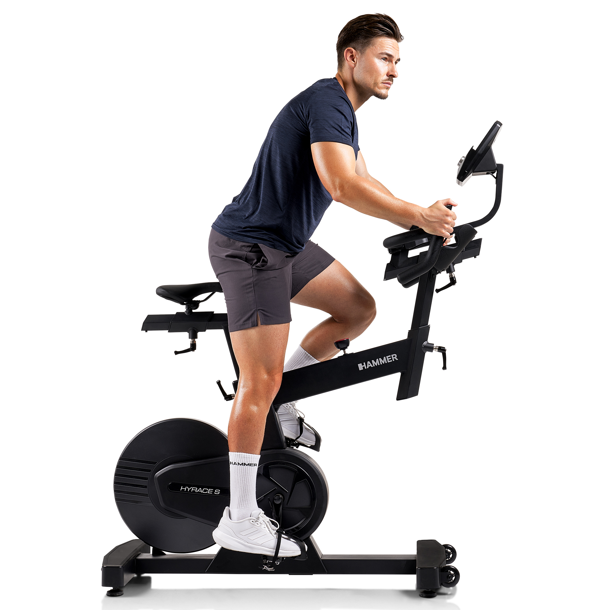 Ein Mann in Shorts und Hemd fährt auf einem schwarzen Heimtrainer Fahrrad und blickt zur Seite. Weißer Hintergrund.