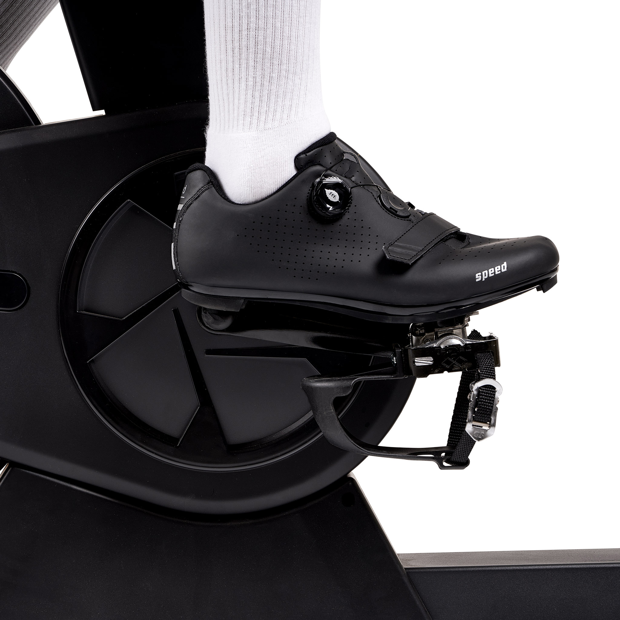 Fuß auf Fahrradpedal. Schwarzer Schuh mit 'speed'-Text. Weißer Strumpf sichtbar. Schwarze Fahrradteile sind im Rahmen.
