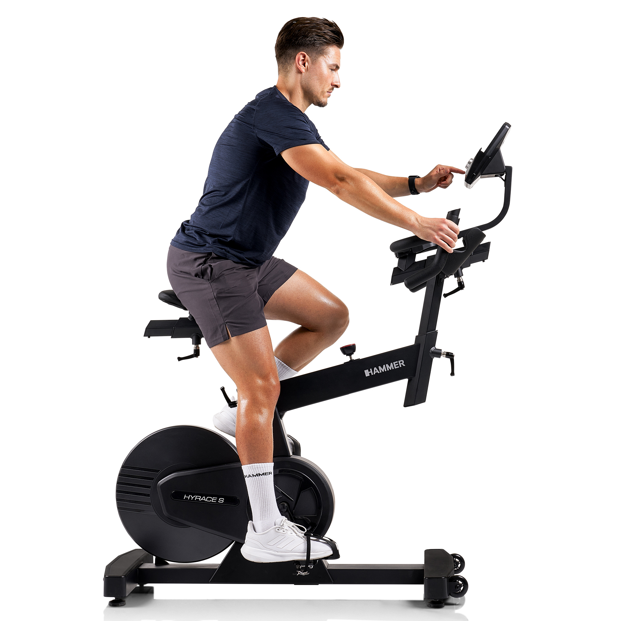 Ein Mann in Sportkleidung sitzt auf einem schwarzen Heimtrainer. Er berührt die Konsole. Das Fahrrad hat die Marke Hammer.