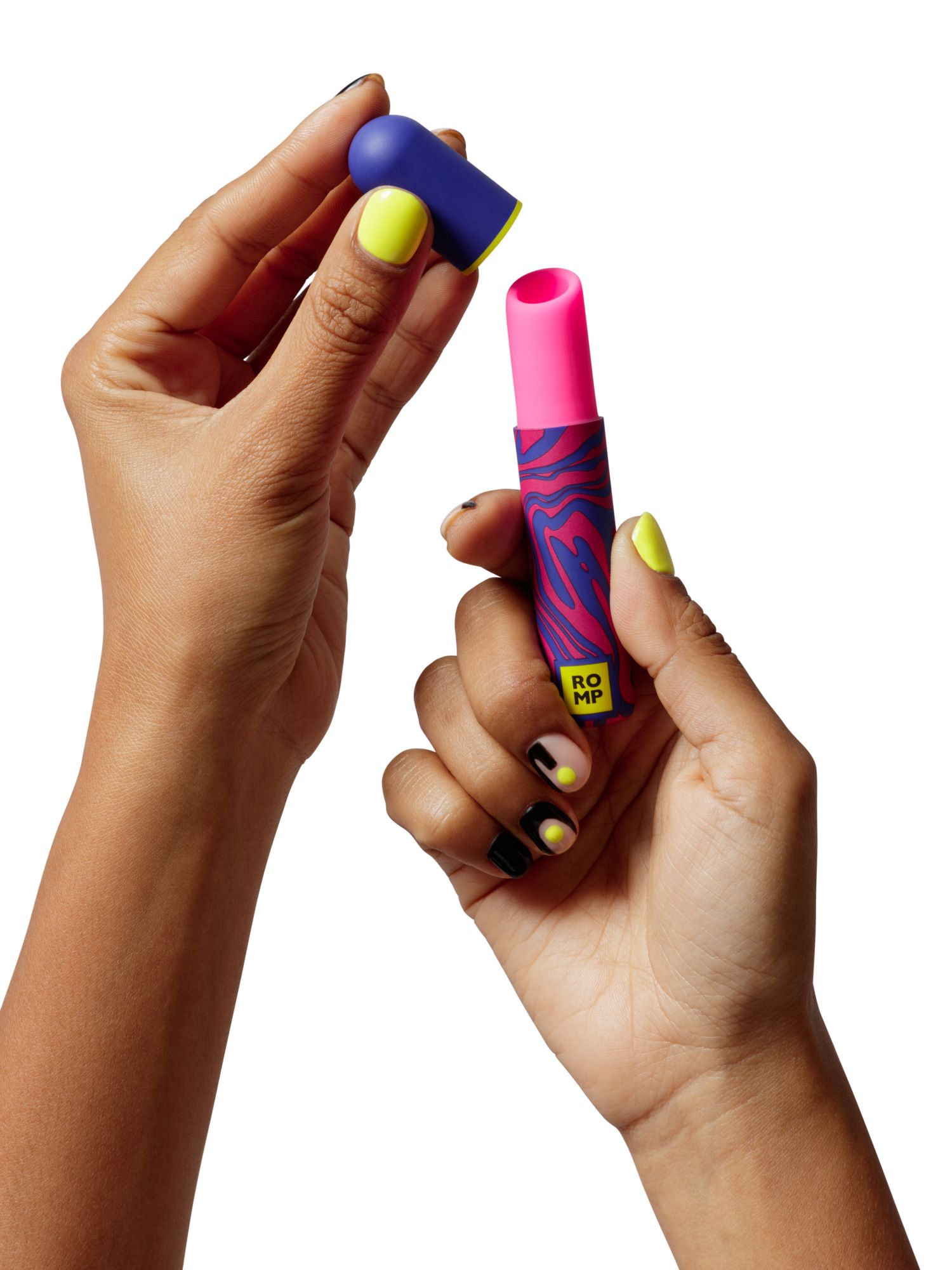 Manos sosteniendo un labial rosa con un tubo estampado azul y rosa. Esmalte de uñas amarillo y negro.