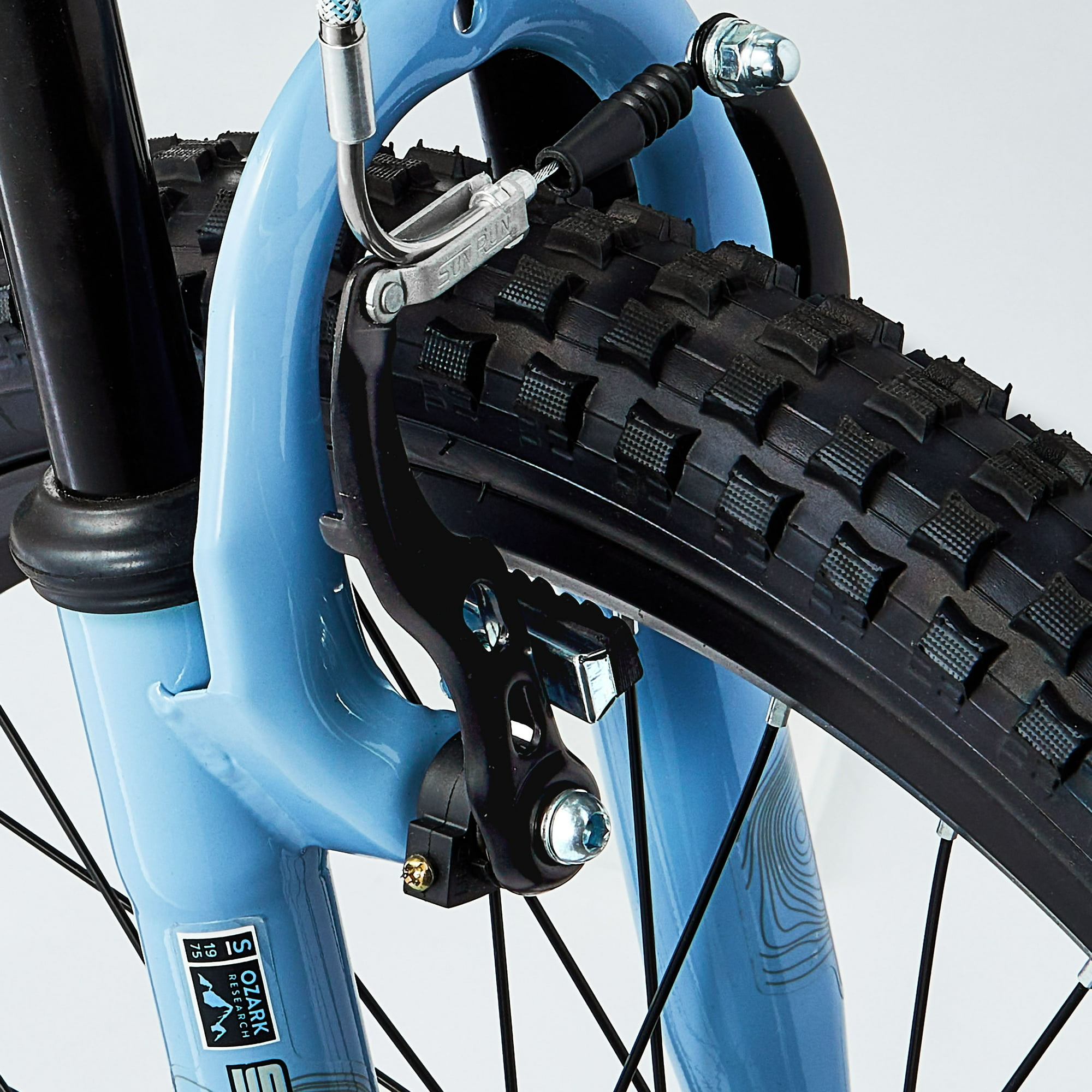 Nahaufnahme eines Fahrradvorderrads. Blaue Gabel, schwarzer Reifen und Bremssystem sind sichtbar. Der Reifen hat ein Profildesign.