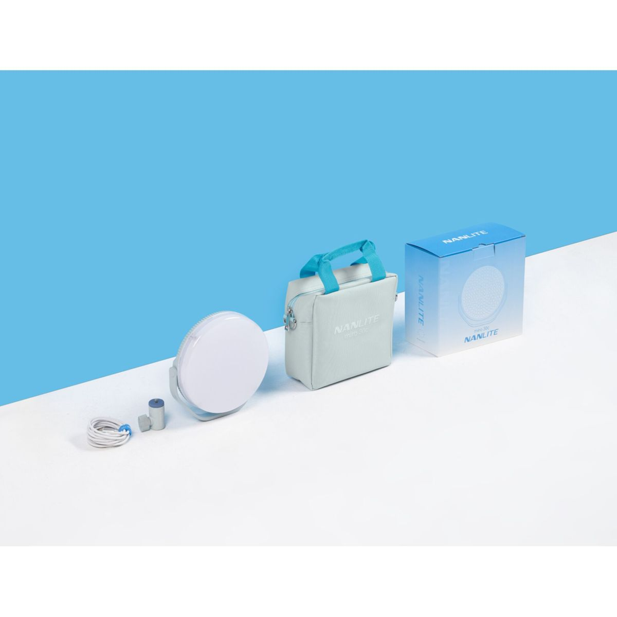 Kit illuminazione studio con luce bianca, borsa grigia e scatola blu su sfondo blu e bianco.