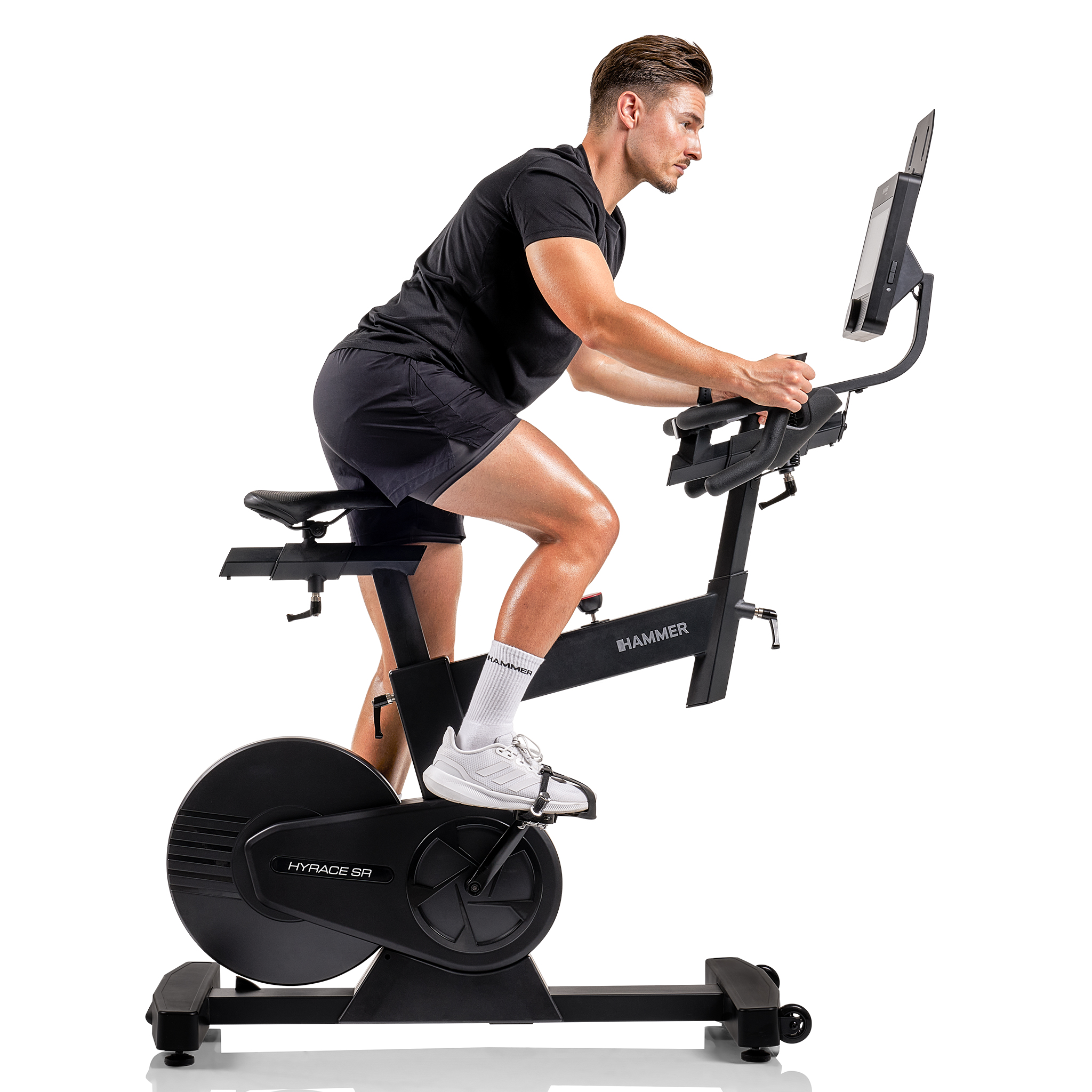 Ein Mann in schwarzer Kleidung fährt auf einem schwarzen Trainingsrad. Das Fahrrad hat einen Bildschirm. Weißer Hintergrund.