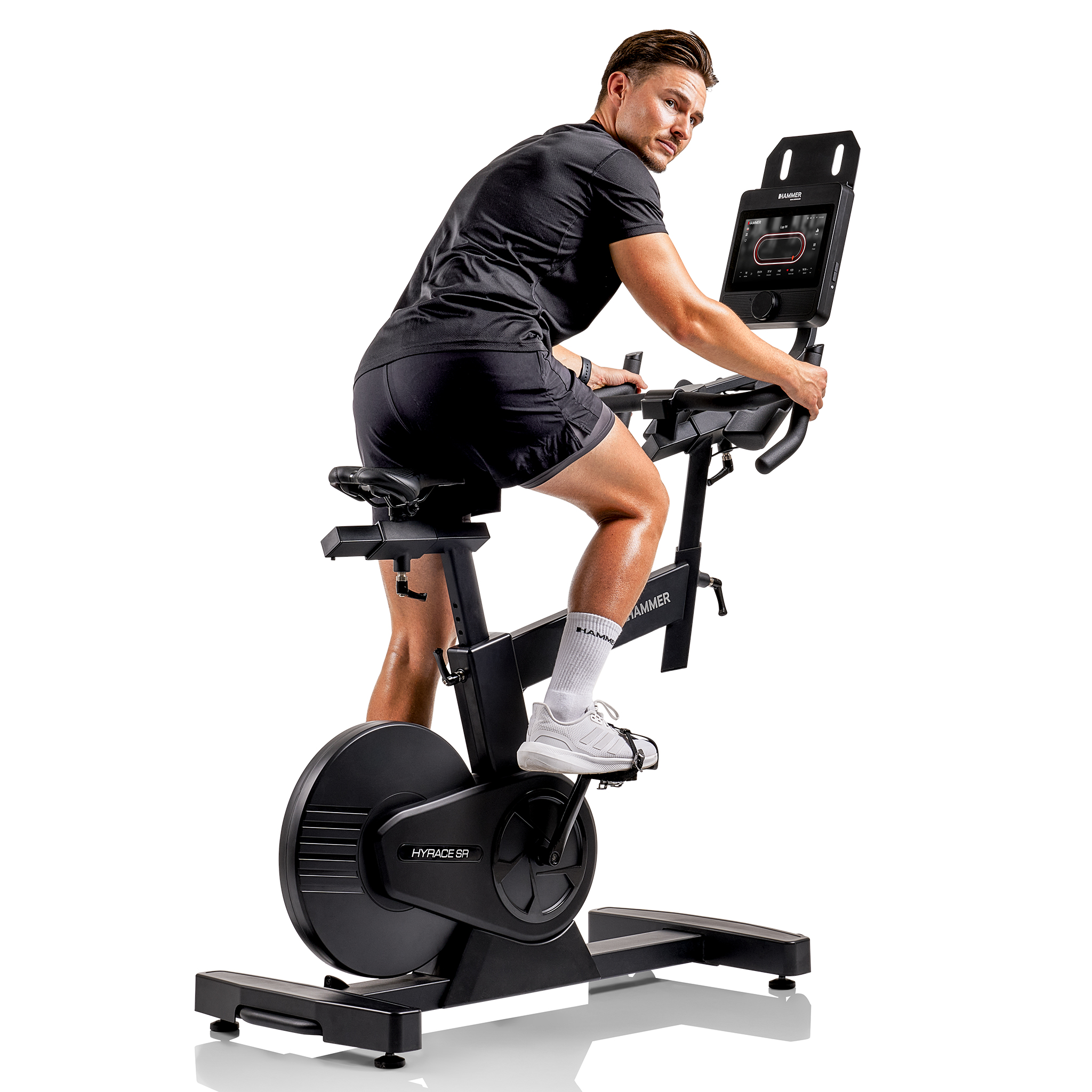 Mann in schwarzer Sportkleidung fährt auf einem Heimtrainer Rad und blickt zurück. Das Fahrrad ist schwarz und hat einen Bildschirm.