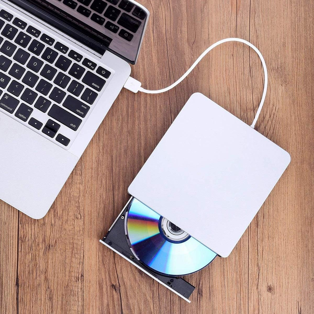 Ein Laptop, der mit einem weißen externen CD/DVD-Laufwerk mit einer Disc verbunden ist, auf einer Holzoberfläche.