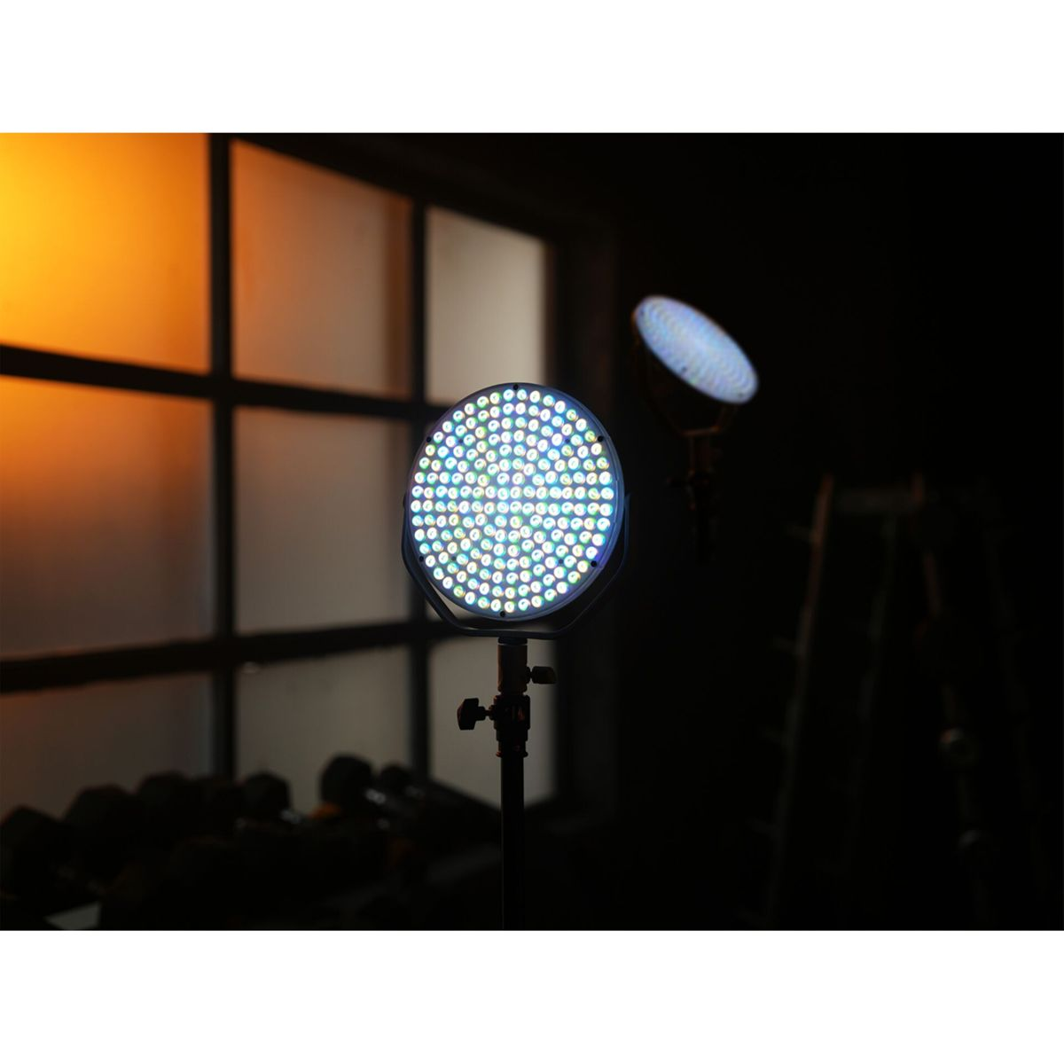 Ein Bühnenlicht mit vielen LEDs steht im Fokus. Ein zweites Licht ist dahinter. Ein Fenster und dunkler Hintergrund sind ebenfalls sichtbar.