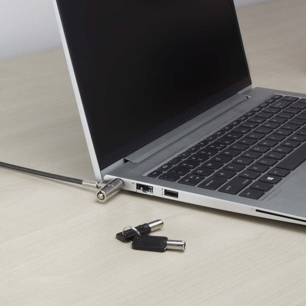 Laptop mit Kabelschloss gesichert. Zwei Schlüssel liegen auf dem Schreibtisch. Der Laptop ist auf einer hellen Holzoberfläche geöffnet.