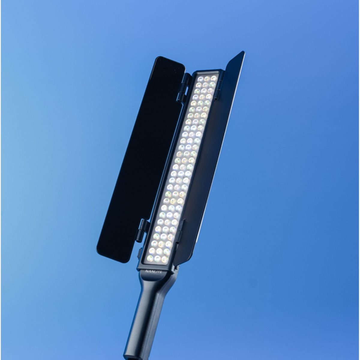 Una luce LED nera con alette laterali aperte contro un cielo blu. La luce è accesa, illuminando molte piccole lampadine.