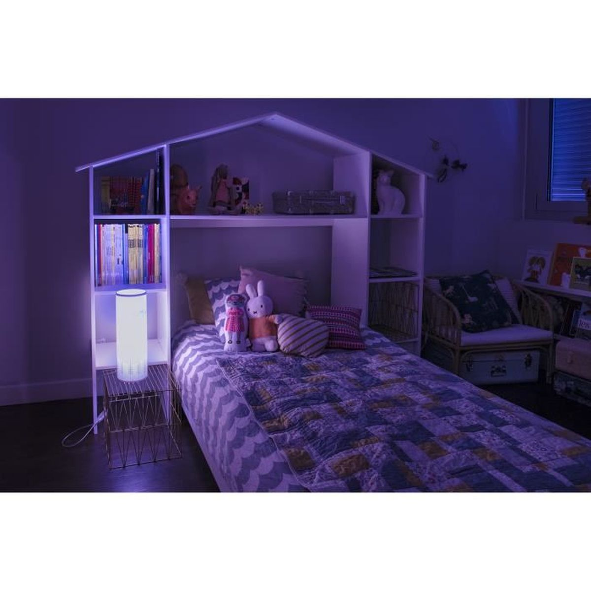 Ein Schlafzimmer mit einem hausförmigen Bettrahmen. Stofftiere auf dem Bett, Bücher in Regalen und eine Lampe. Der Raum hat einen bläulichen Farbton.