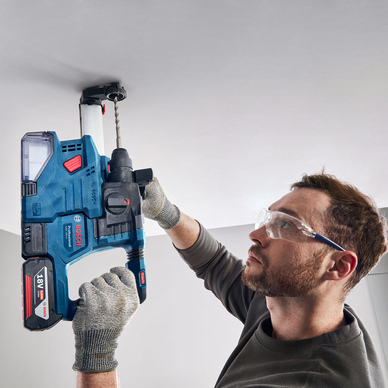 Ein Mann bohrt mit einem blauen Bosch-Bohrer in eine weiße Decke. Er trägt eine Schutzbrille und Handschuhe.