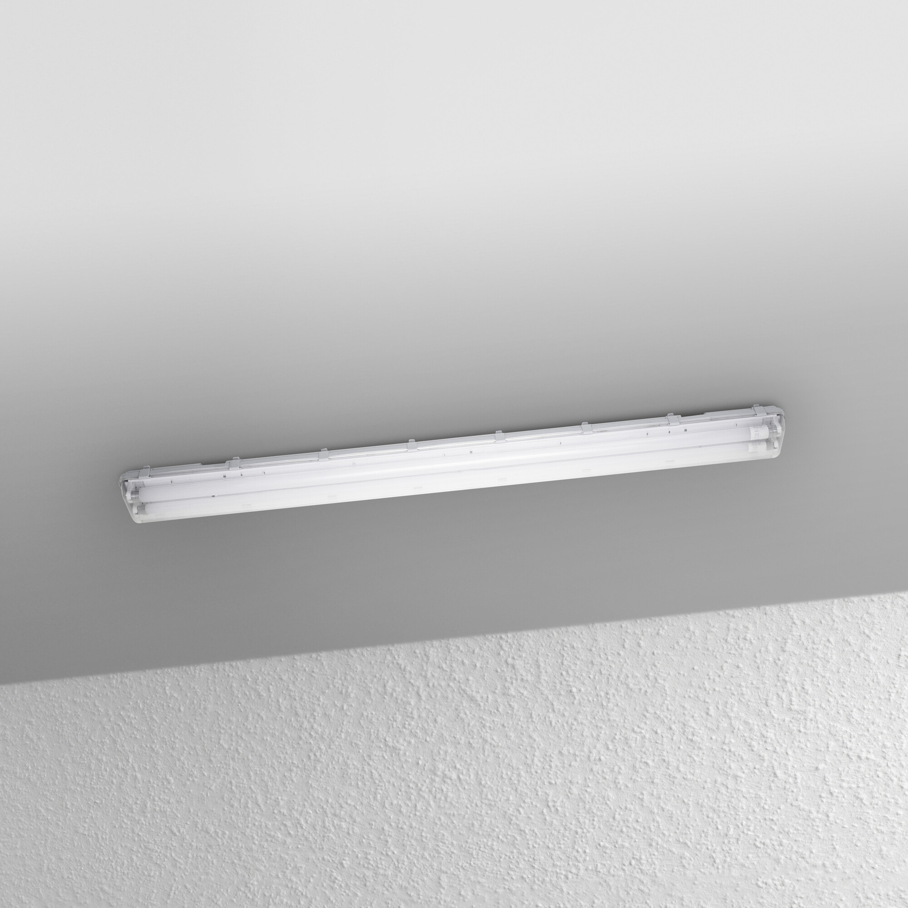 Un apparecchio di illuminazione fluorescente è montato a soffitto. Lo sfondo è un muro bianco.