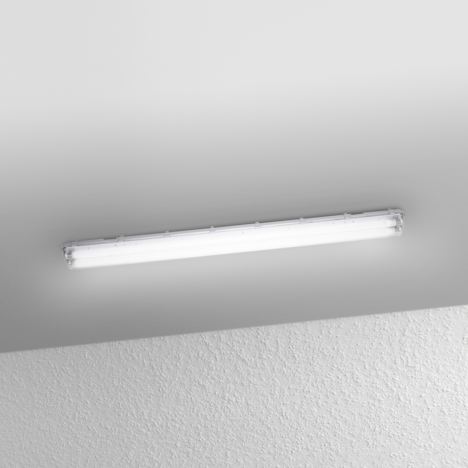 Un apparecchio di illuminazione a fluorescenza è montato su un soffitto. Il soffitto è bianco, il muro è strutturato.
