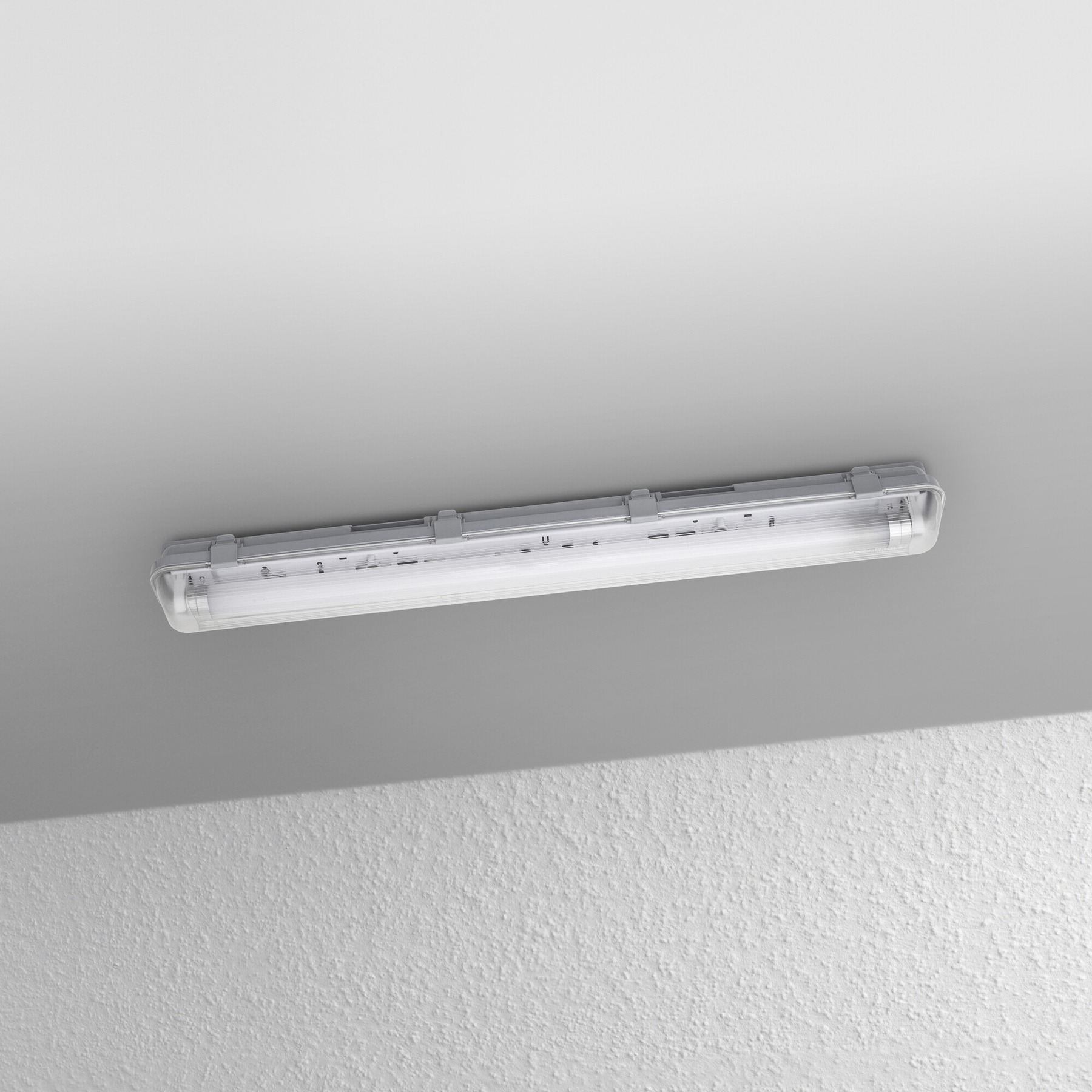 Eine Leuchtstoffröhre ist an der Decke montiert. Der Hintergrund ist eine strukturierte Wand. Das Licht ist an.