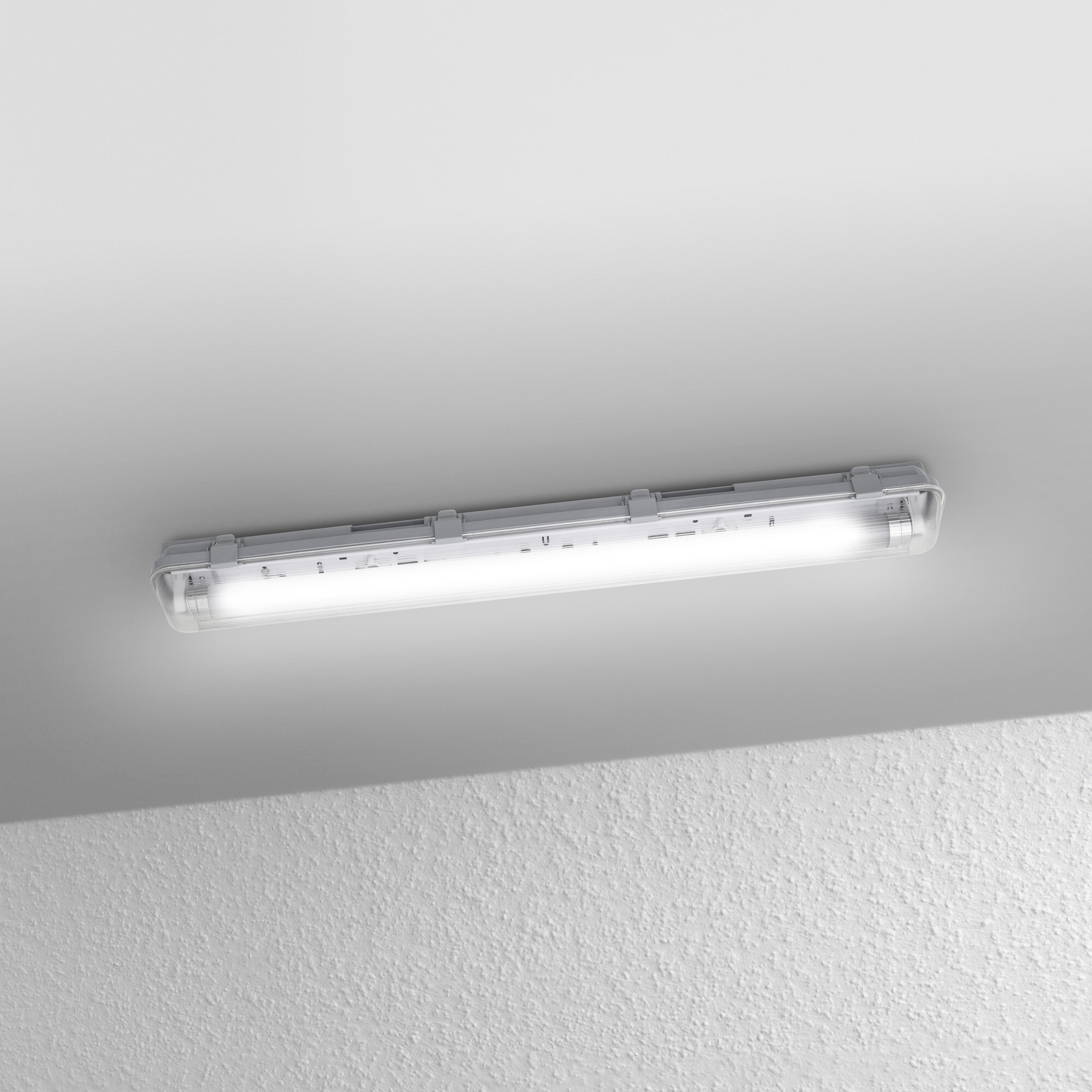 Eine Leuchtstoffröhre ist an einer weißen Decke montiert. Die Wand hat eine raue Textur mit einem Schatten darauf.