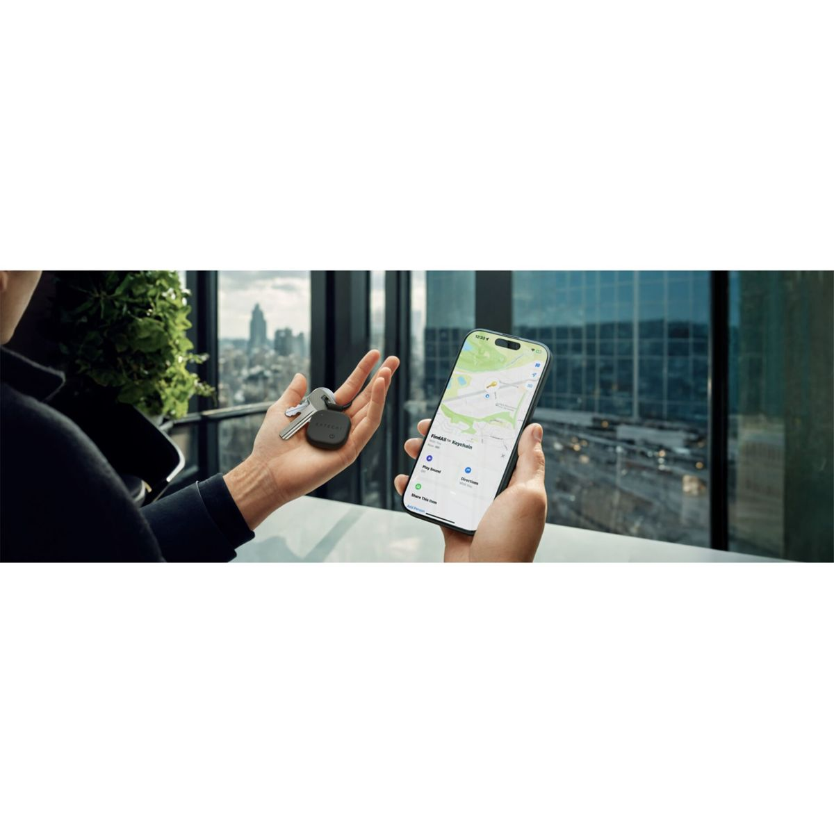 Eine Person hält Schlüssel und einen Tracker sowie ein Smartphone mit einer Karte. Im Hintergrund sind Stadtgebäude zu sehen.