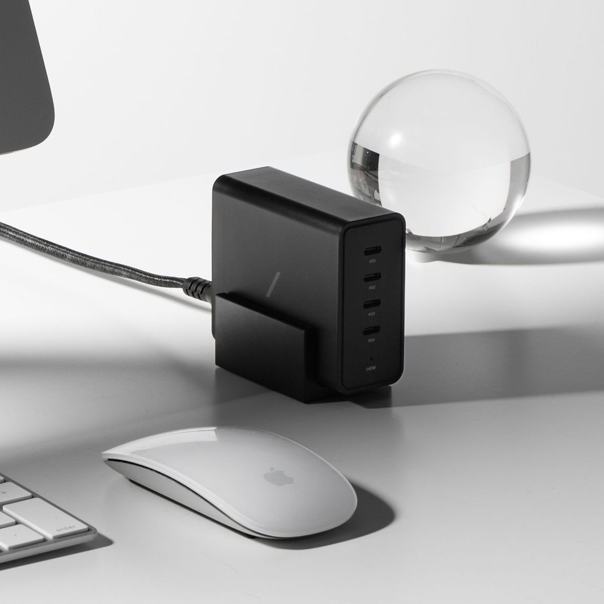 Une station de recharge noire avec plusieurs ports, une souris Apple blanche et une sphère de verre sur une surface blanche.