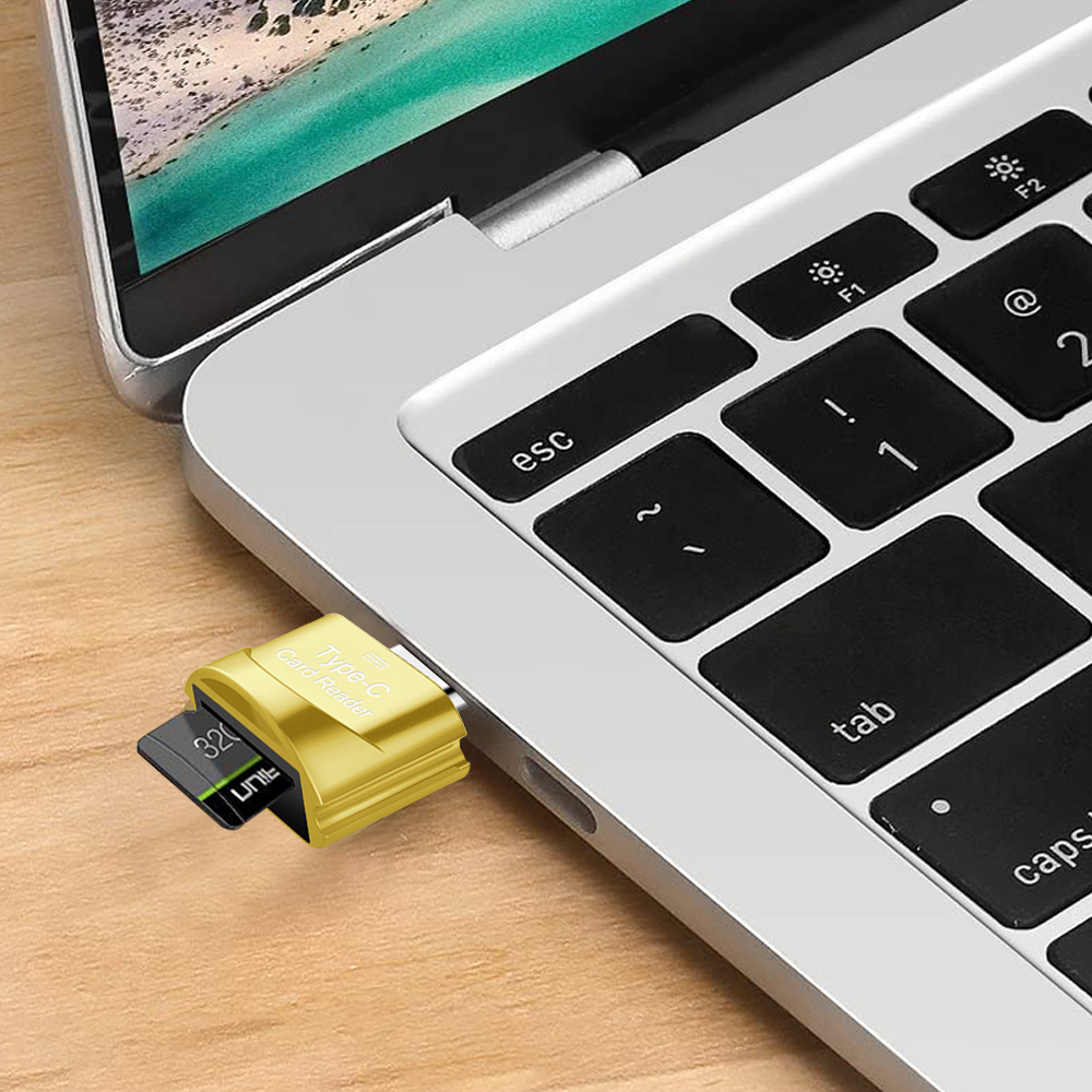 Ein goldener Typ-C-Kartenleser ist an einen Laptop angeschlossen. Eine schwarze SD-Karte ist eingesetzt. Die Laptop-Tastatur ist sichtbar.