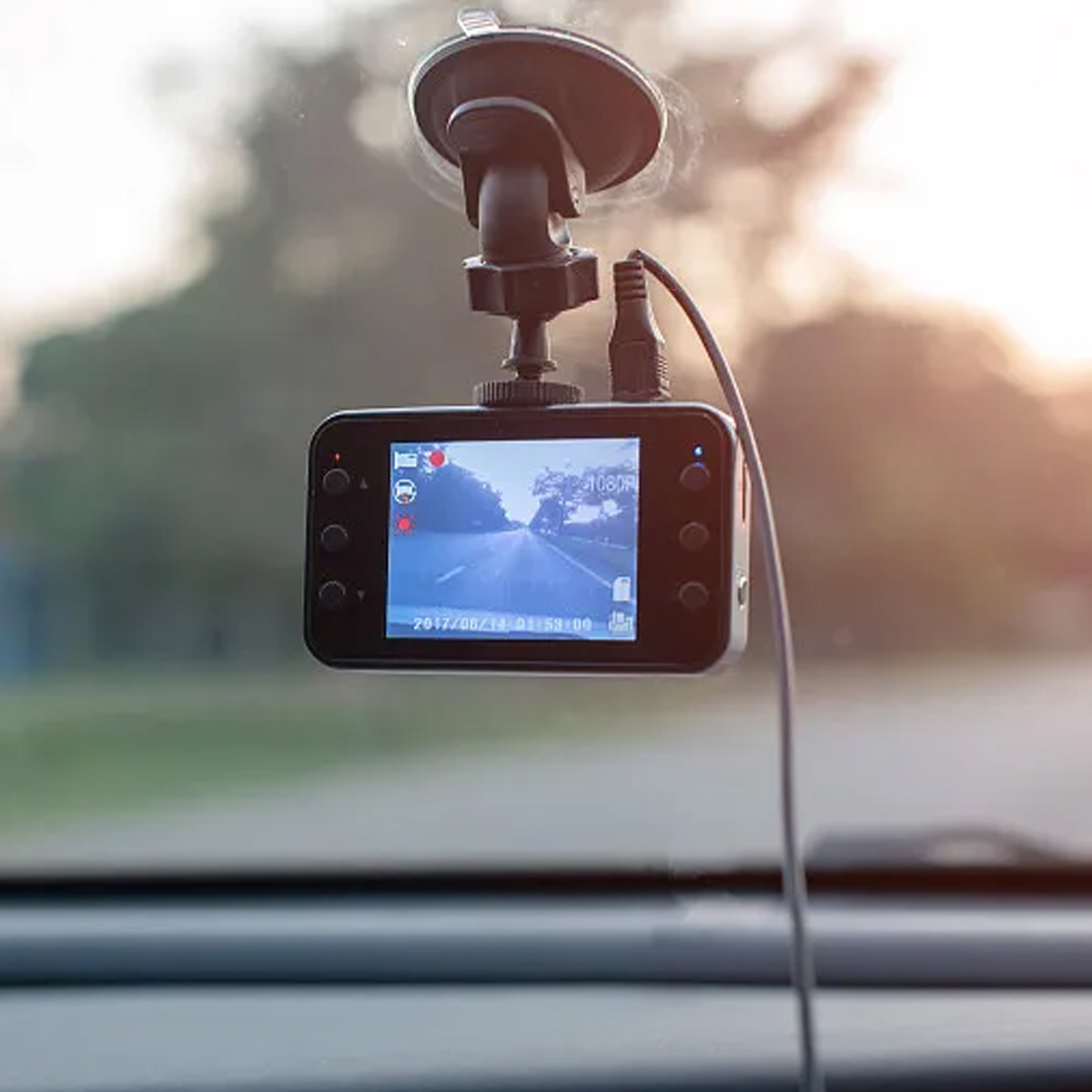 Eine Dashcam ist an der Windschutzscheibe eines Autos befestigt und zeigt die Straßenansicht. Die Szene ist von innen im Auto gerahmt, mit unscharfem Hintergrund.