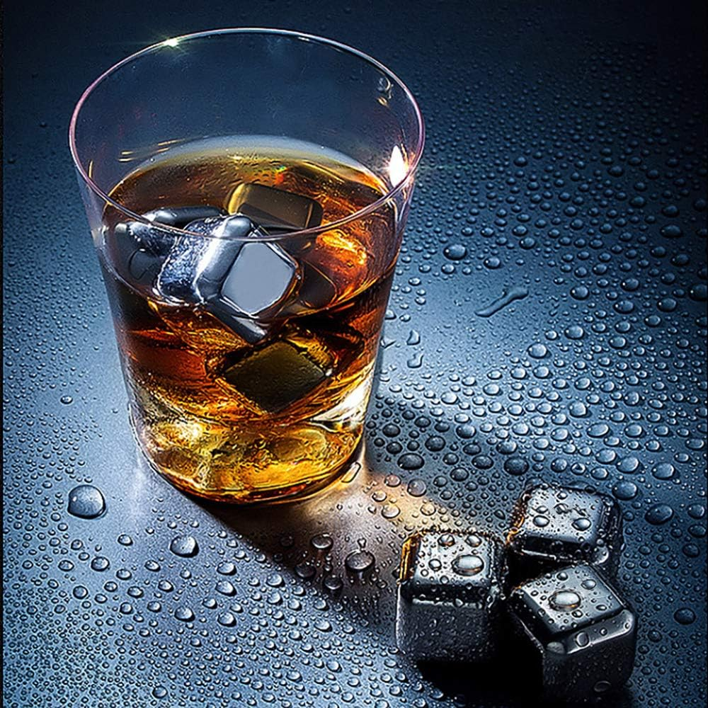 Ein Glas Whiskey mit Metall-Eiswürfeln. Wassertropfen bedecken die Oberfläche. Drei weitere Würfel liegen neben dem Glas.