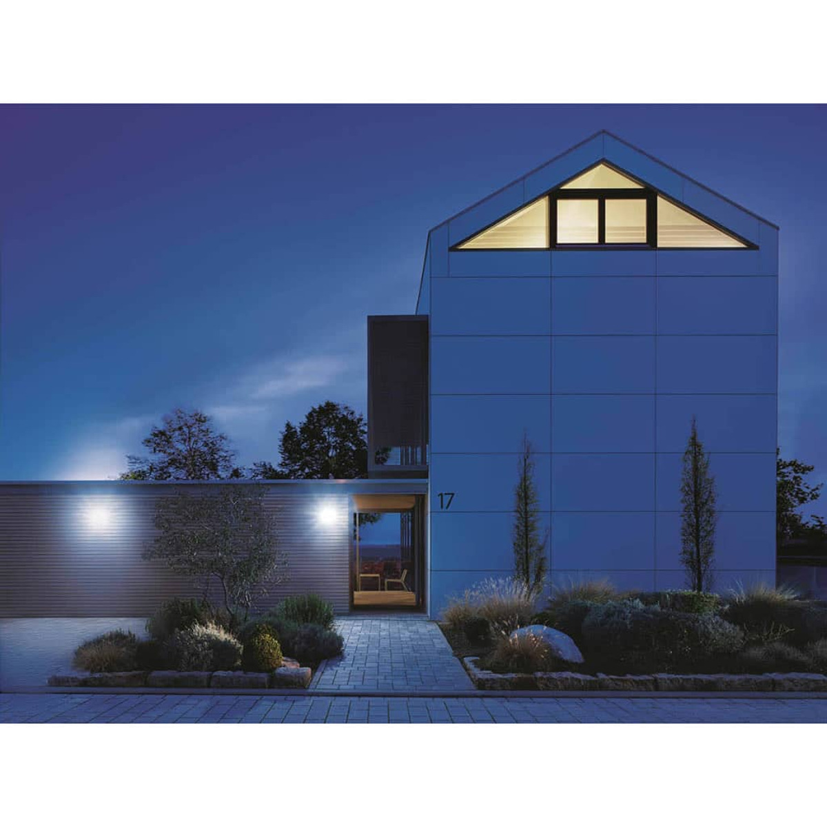 Modernes blaues Haus mit dreieckigem Fenster. Nummer 17. Landschaftsbau mit Büschen und kleinen Bäumen. Dunkelblauer Himmel in der Abenddämmerung.
