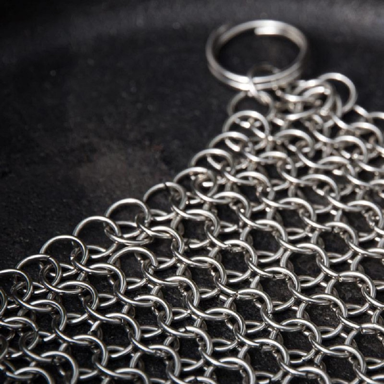 Nahaufnahme von Kettenhemd auf dunkler Oberfläche. Das Kettenhemd ist silber und glänzend. Der Hintergrund ist dunkel und strukturiert.