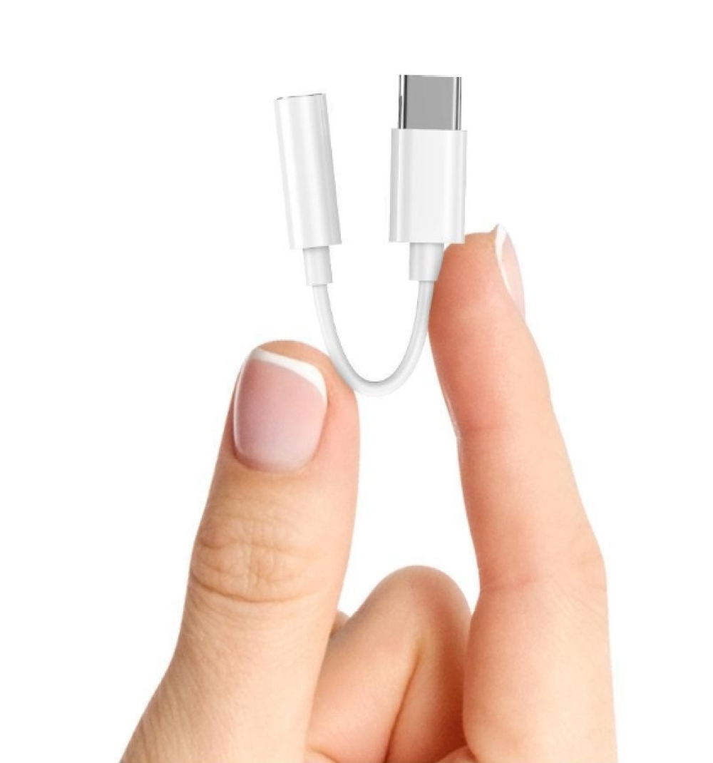 Ein weißer USB-C-auf-Kopfhöreranschluss-Adapter, der von einer Hand mit gepflegten Nägeln vor weißem Hintergrund gehalten wird.