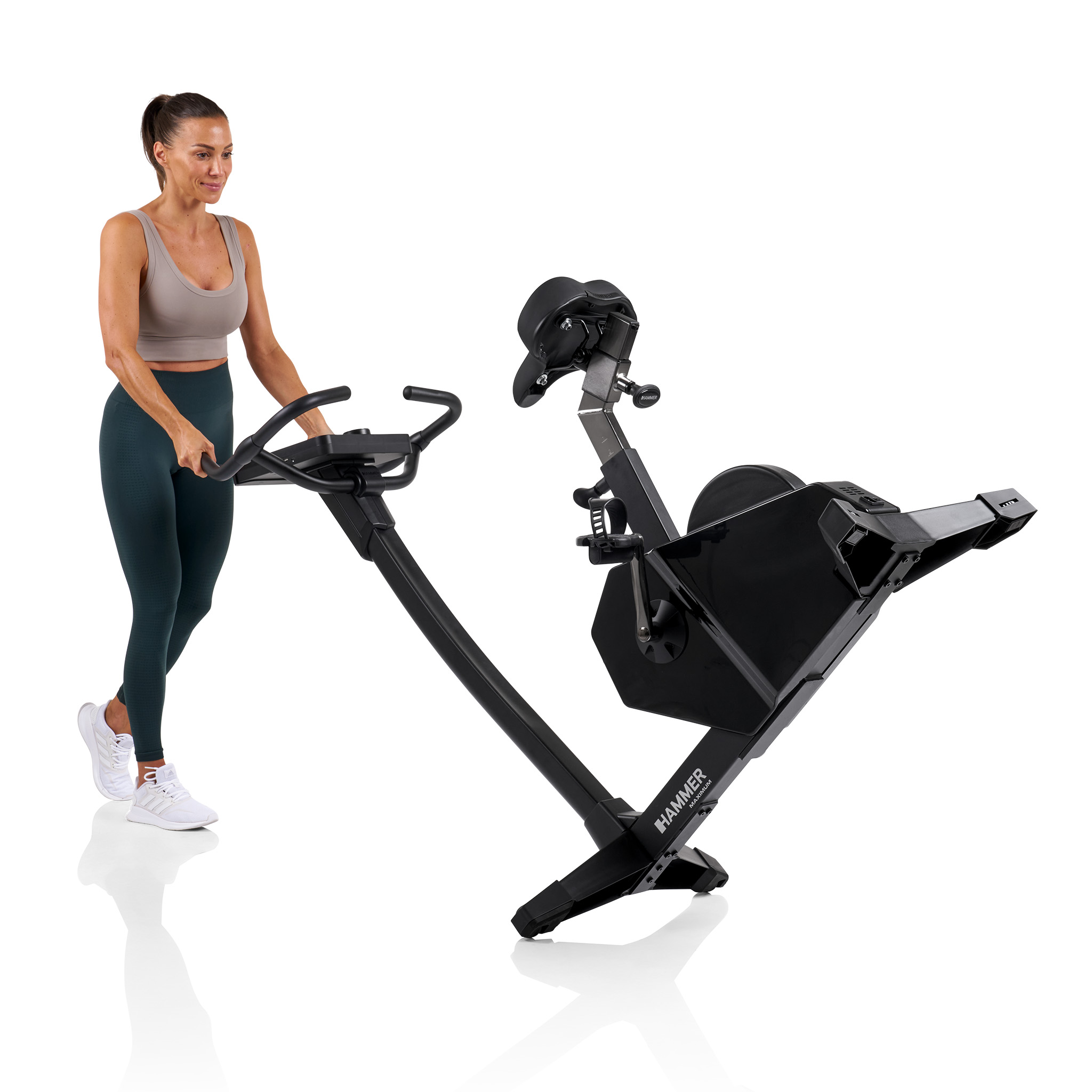 Eine Frau trainiert mit einem schwarzen Heimtrainer. Sie trägt einen Sport-BH, Leggings und weiße Schuhe.
