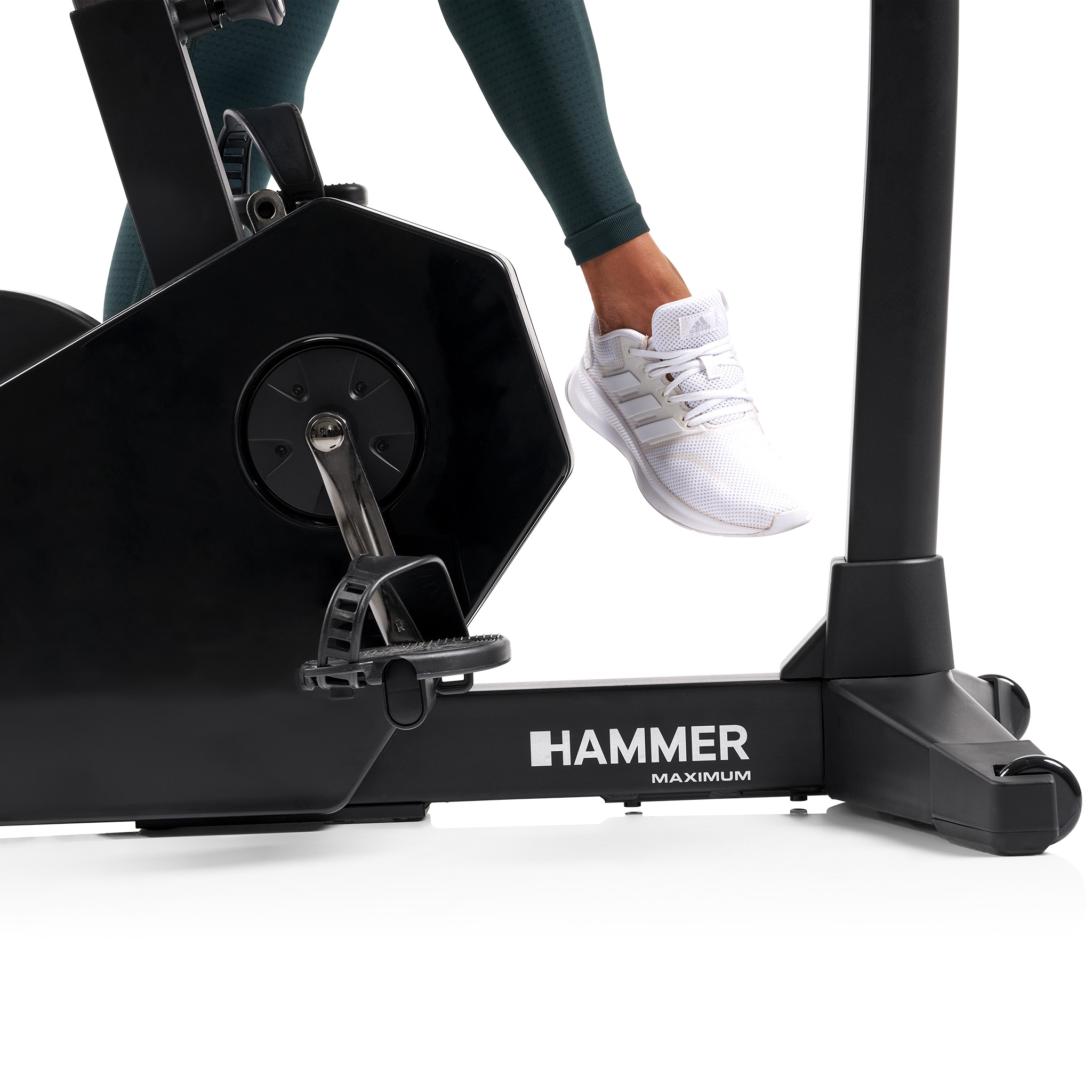 Bein in grünen Leggings und weißem Schuh tritt auf einem schwarzen Heimtrainer. Auf dem Rad steht HAMMER MAXIMUM.