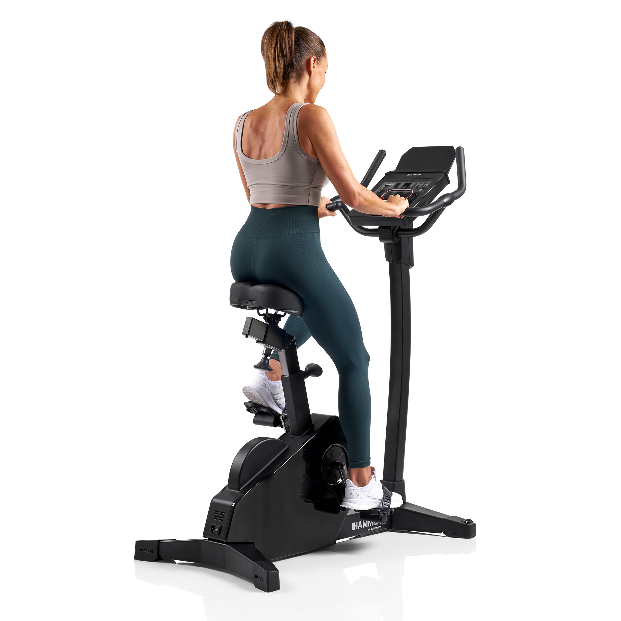 Frau auf Heimtrainer, Sportkleidung. Das Fahrrad ist schwarz. Weißer Hintergrund.