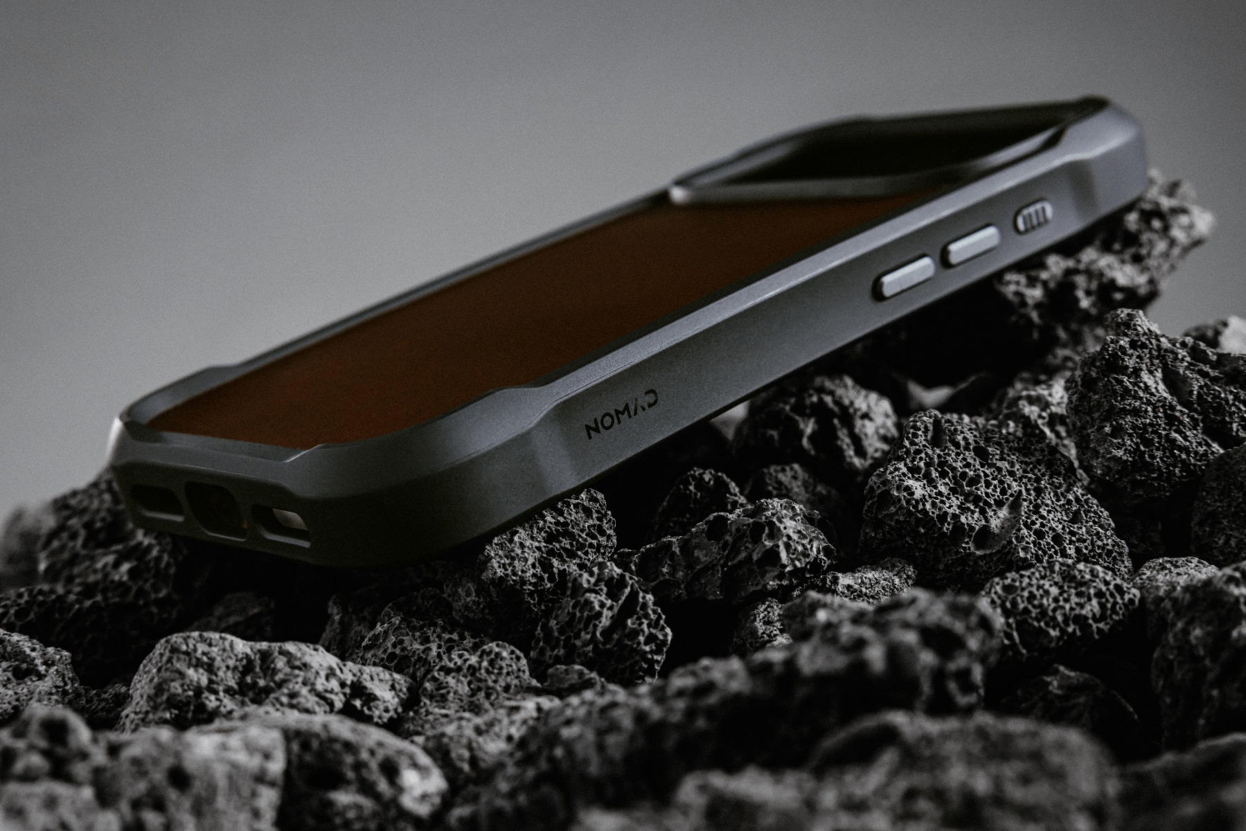 Una custodia per telefono con pelle e cornice nera è posizionata su rocce scure e strutturate. Sulla custodia c'è la parola NOMAD.