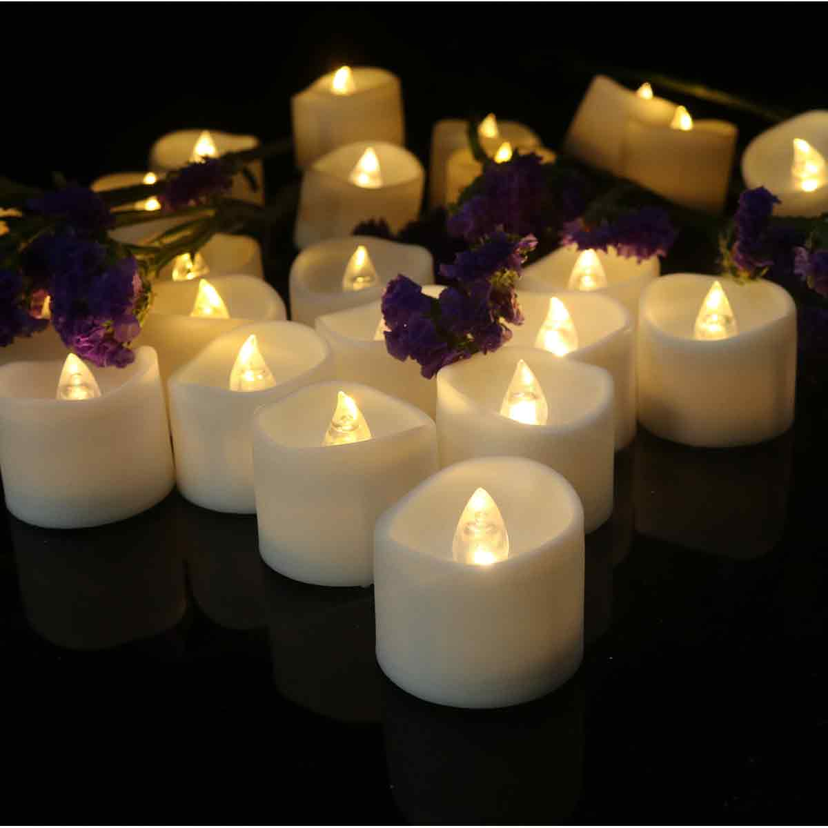 Nahaufnahme von weißen LED-Kerzen mit brennenden Flammen, lila Blumen. Schwarzer Hintergrund. Die Kerzen sind eng angeordnet.