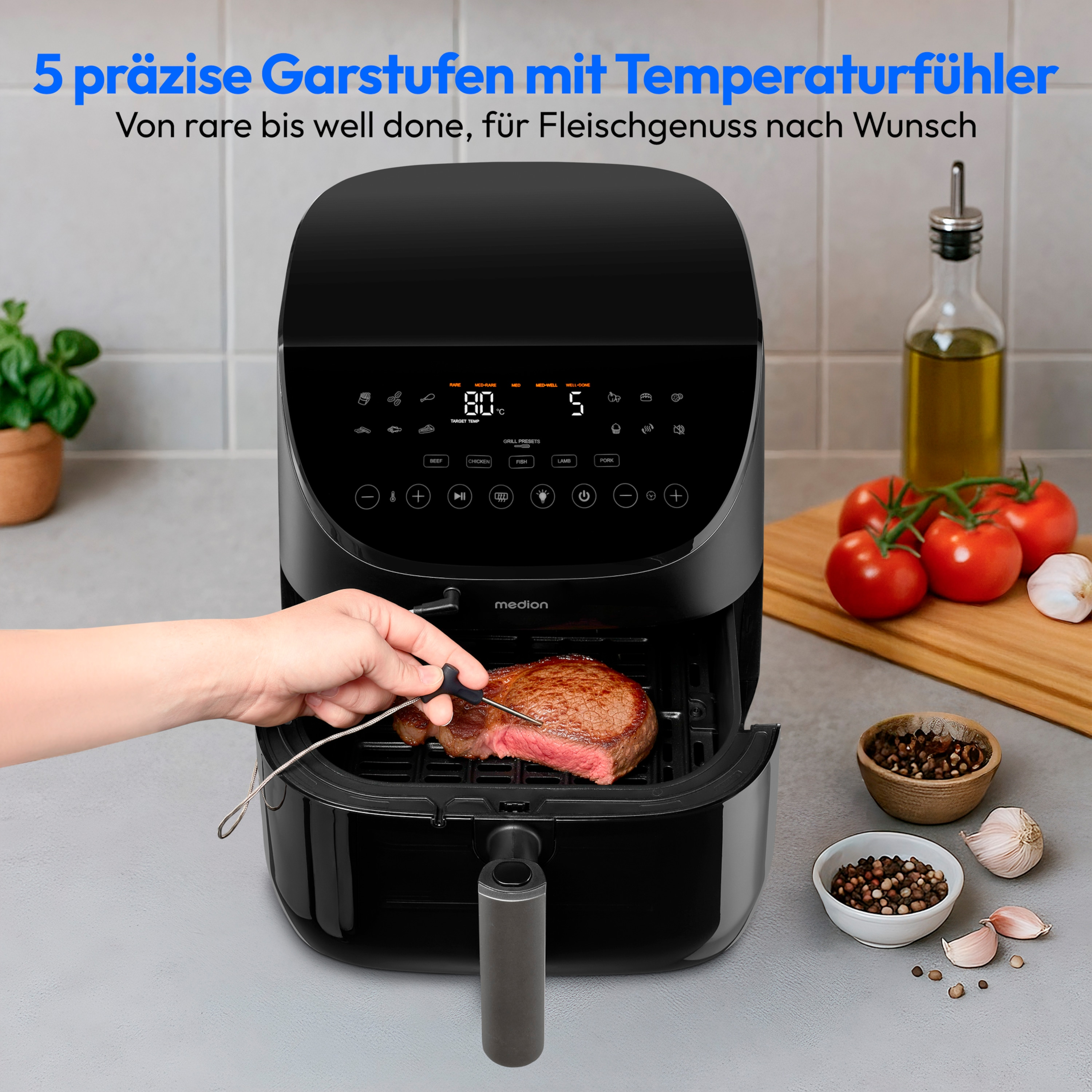 Een zwarte airfryer met een biefstuk erin. Een hand houdt een vleesthermometer vast. Tomaten en kruiden op de achtergrond.