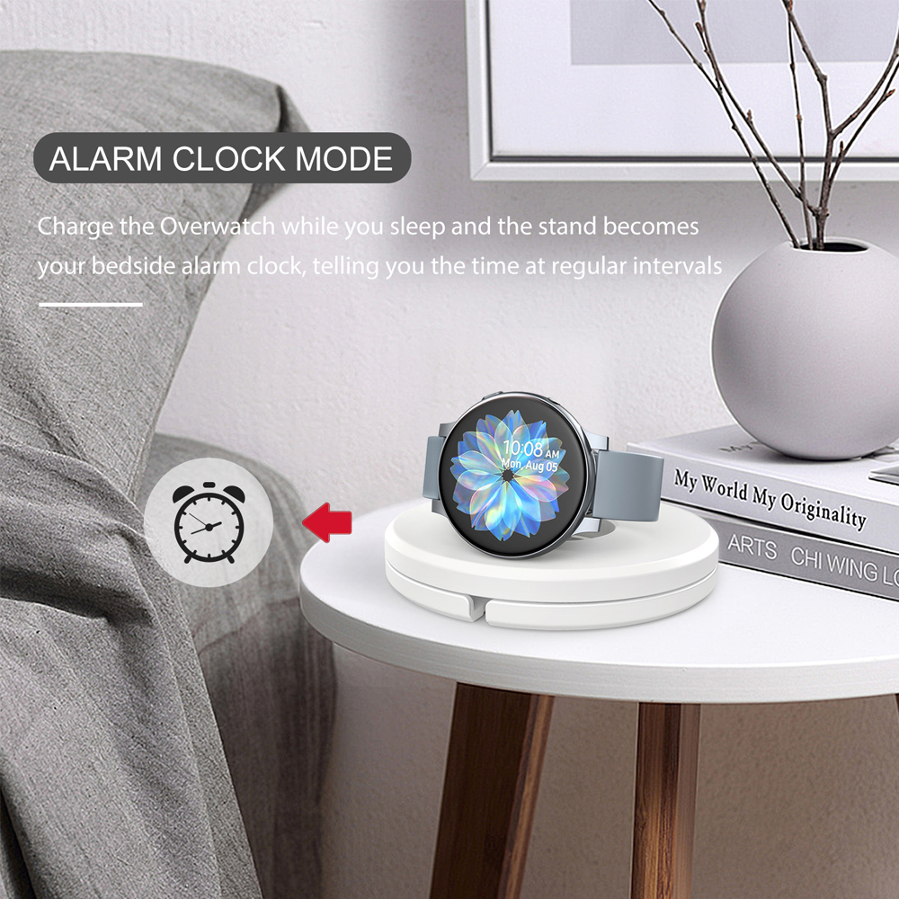 Eine Smartwatch auf einem weißen Ladeständer auf einem weißen Tisch. Ein Wecker-Symbol und der Text 'ALARM CLOCK MODE' sind sichtbar.