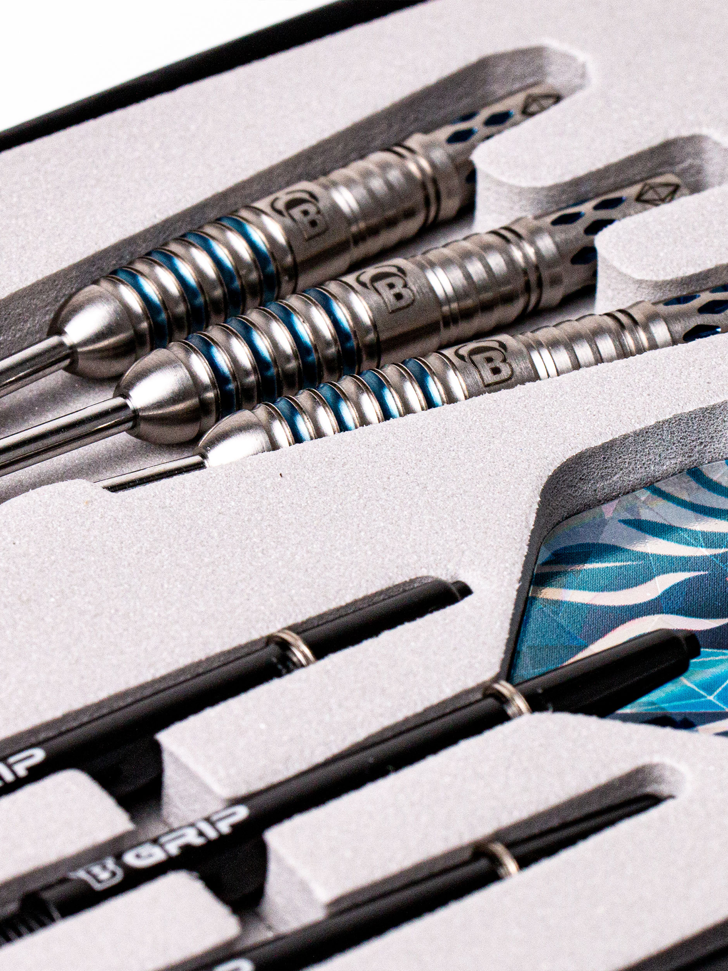 Nahaufnahme eines Dart-Sets in einer schwarzen Box. Darts sind silberfarben mit blauen Ringen. Schwarze Dartpfeilschäfte unten.