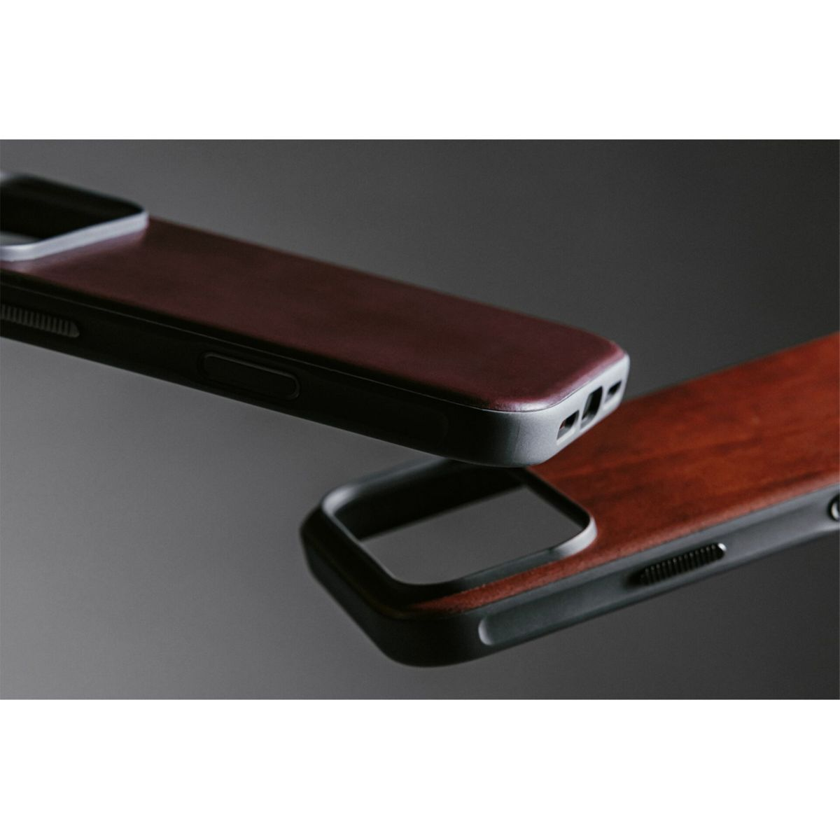 Due custodie per telefoni. Una con cornice nera e retro bordeaux effetto legno. L'altra simile, entrambe su superficie grigia.