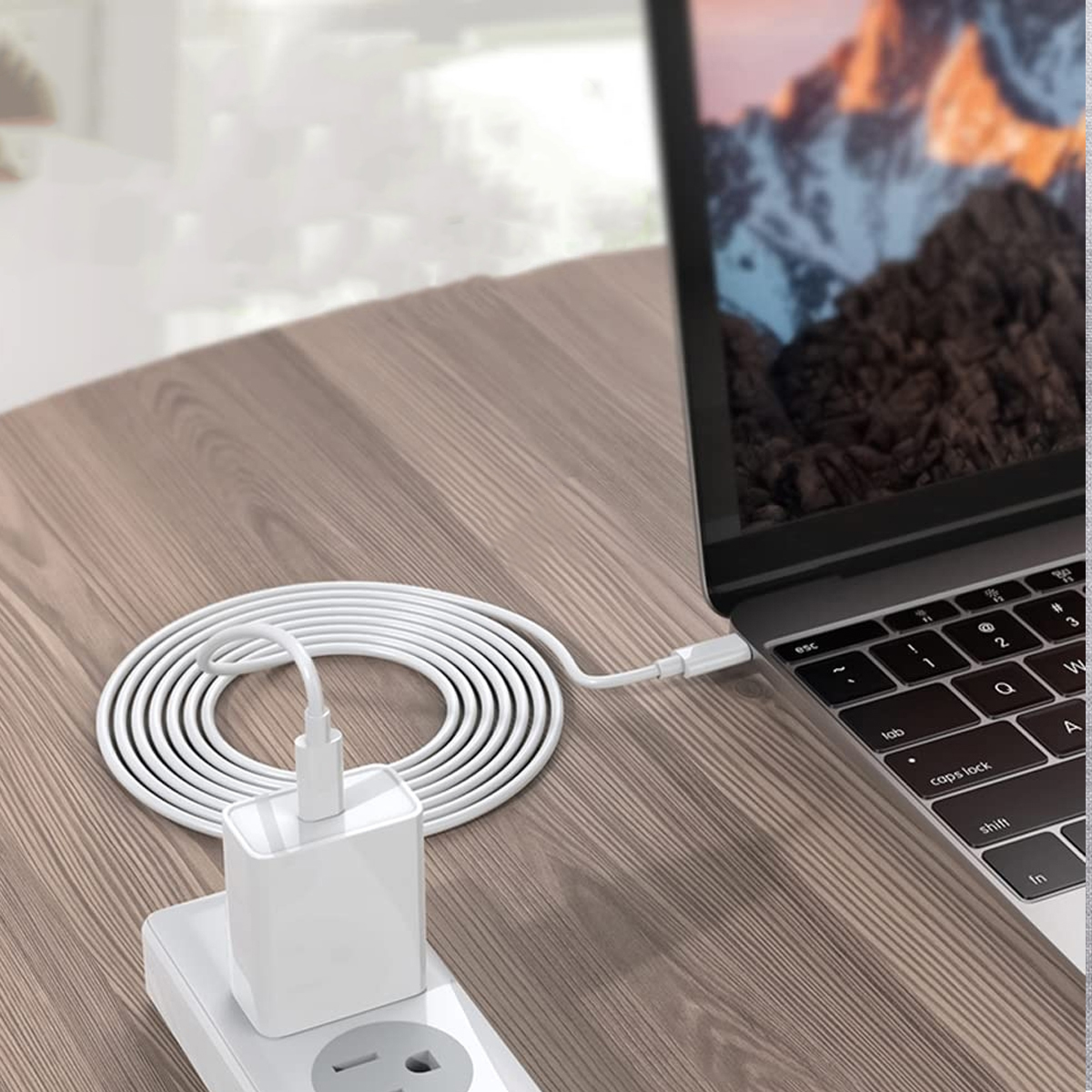 Ein weißes Laptop-Ladegerät ist an einen Laptop auf einem Holztisch angeschlossen. Das Ladegerät ist an eine Steckdose angeschlossen.